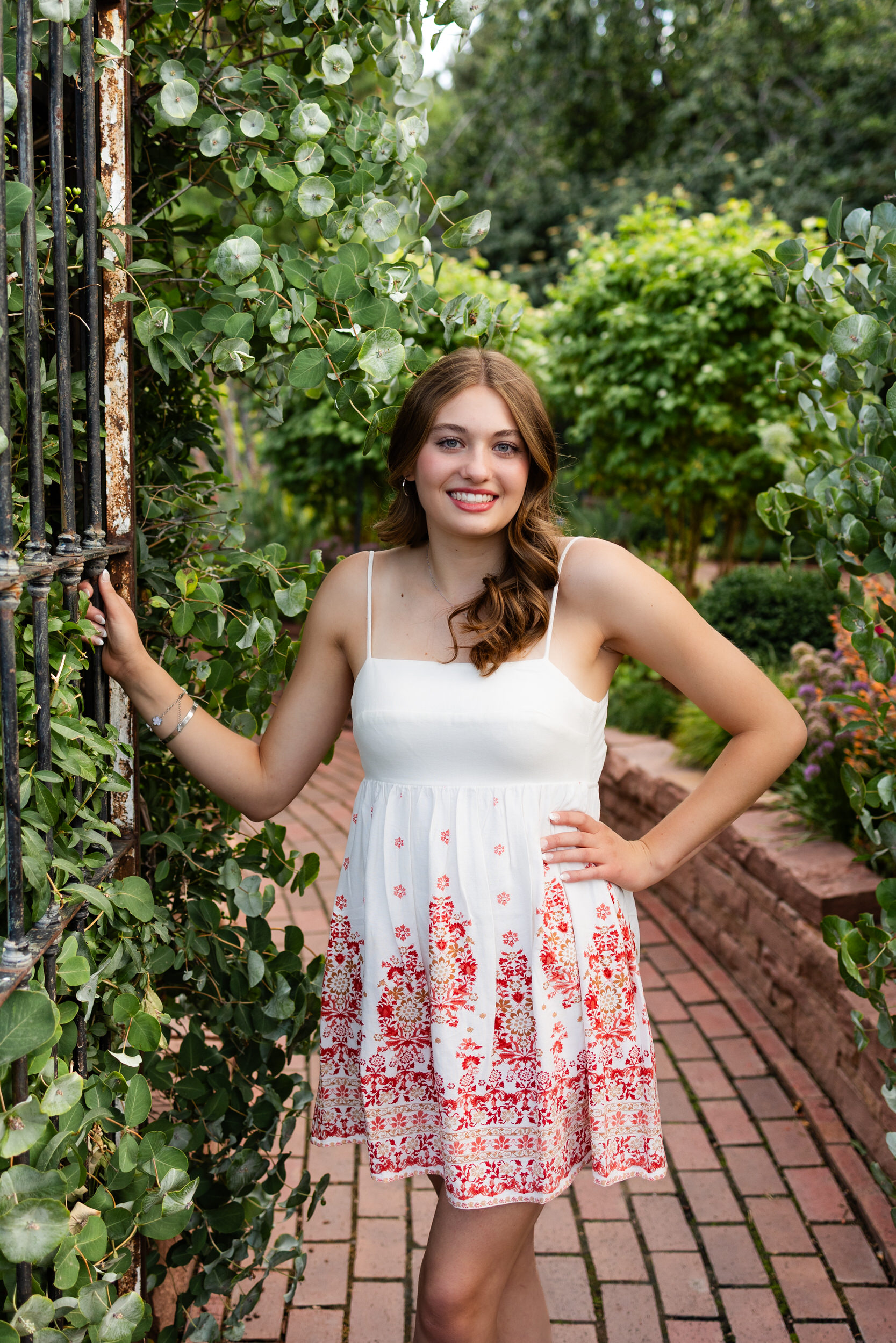 A young woman stands under a garden gate and smiles at the camera.