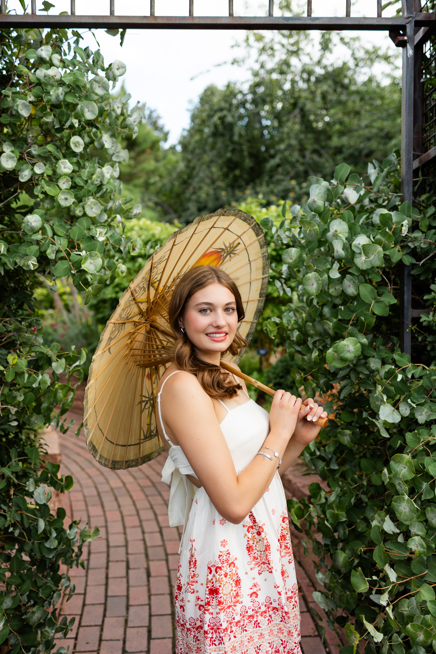 A young woman holding a parasol smiles at the camera.
