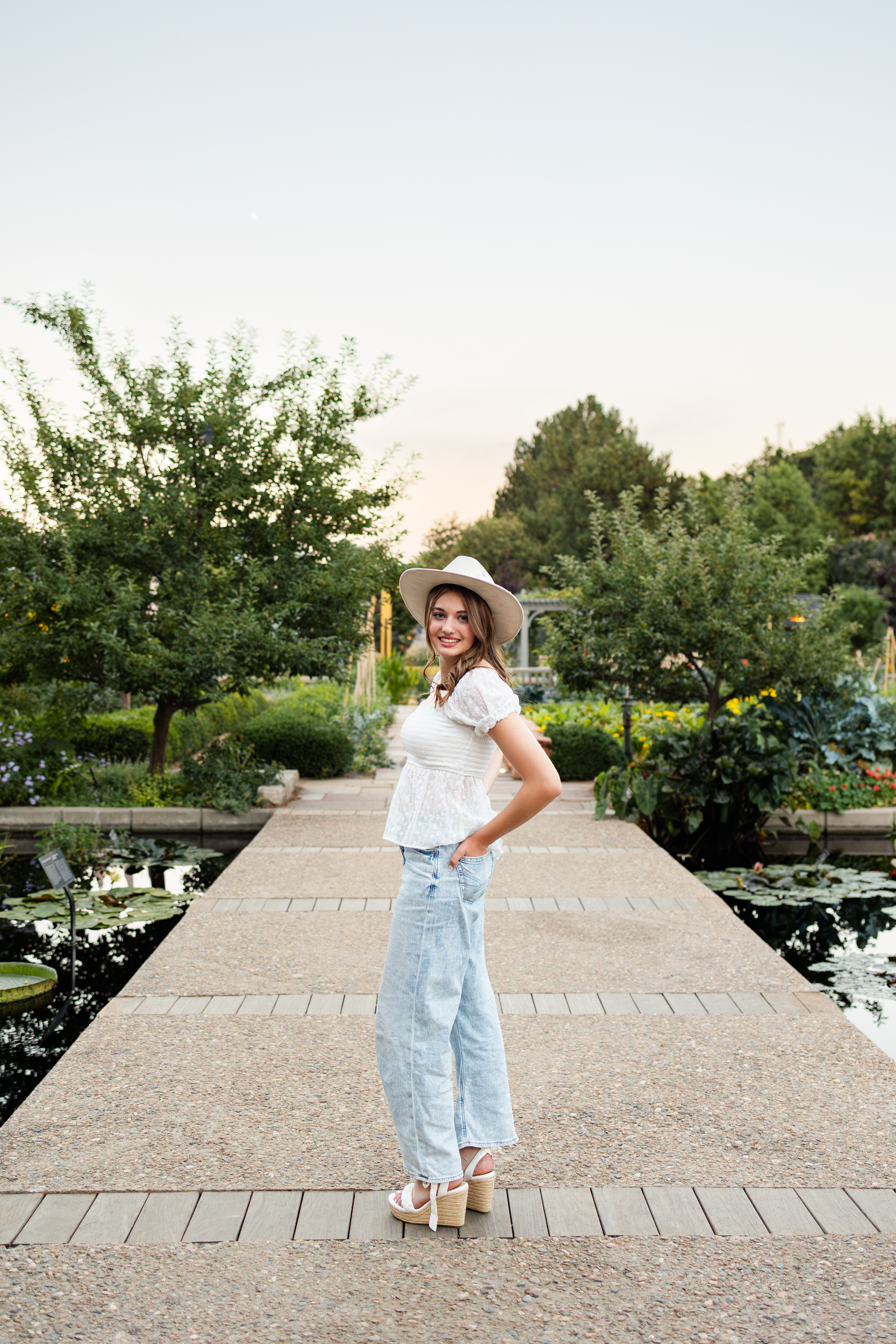 A young woman stands on a bridge over a pond and smiles at the camera.
