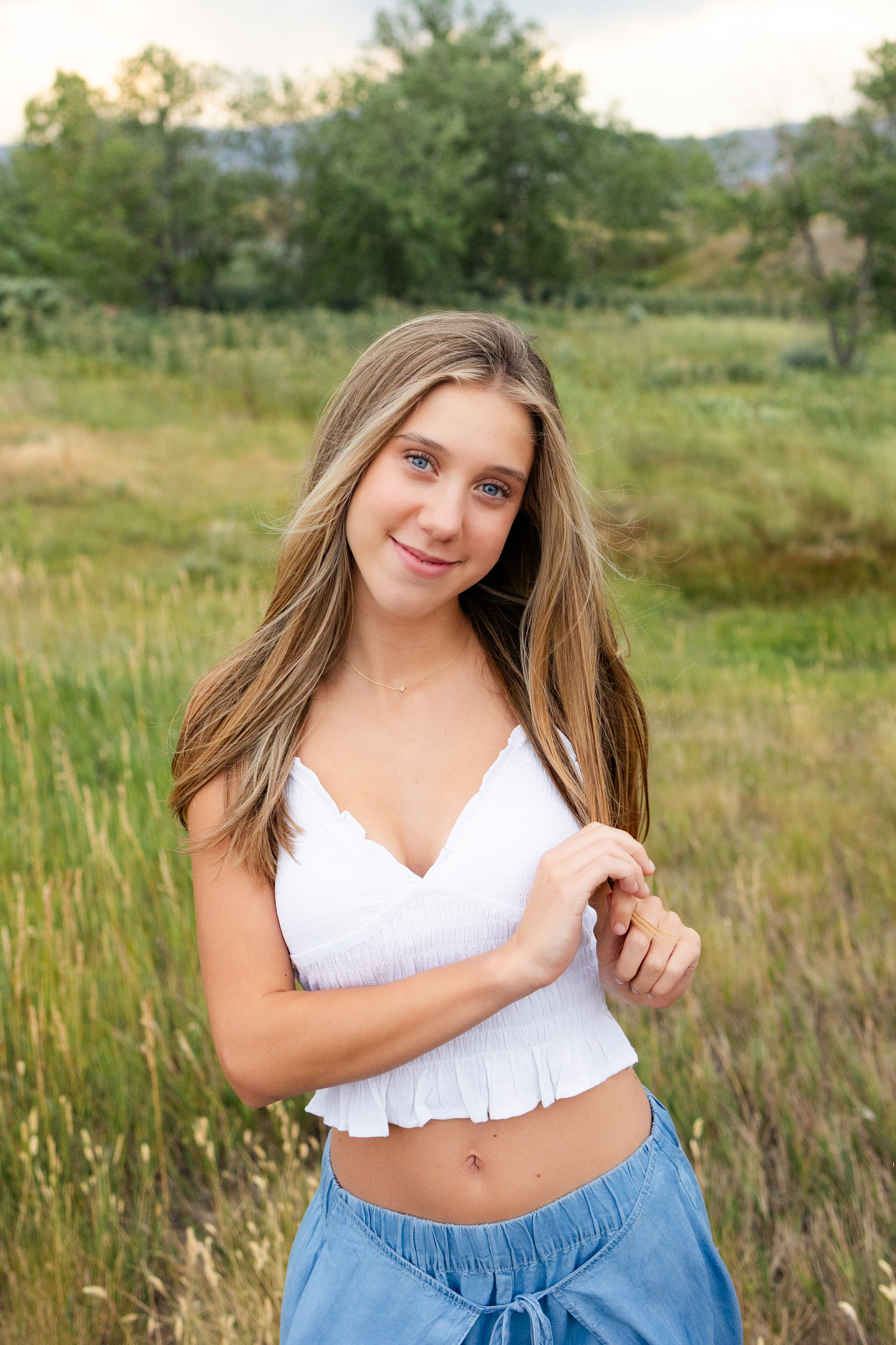 A young woman runs her hands through her hair and smiles at the camera.