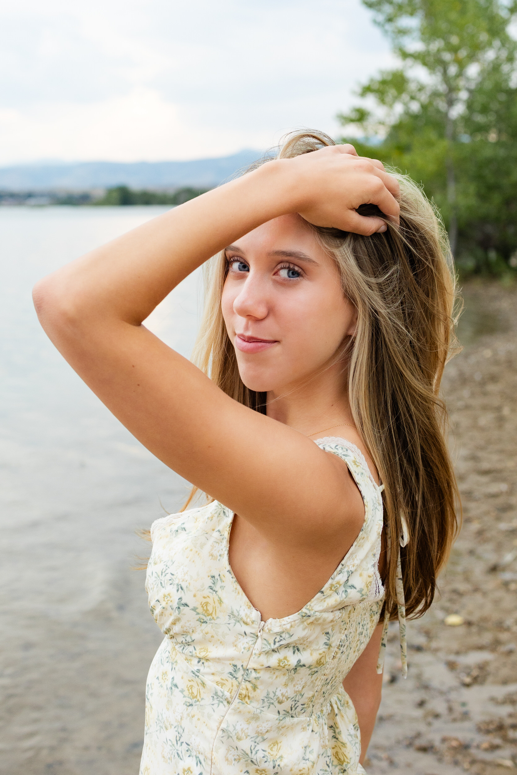 A young woman stands on a beach and runs her hand through her hair.