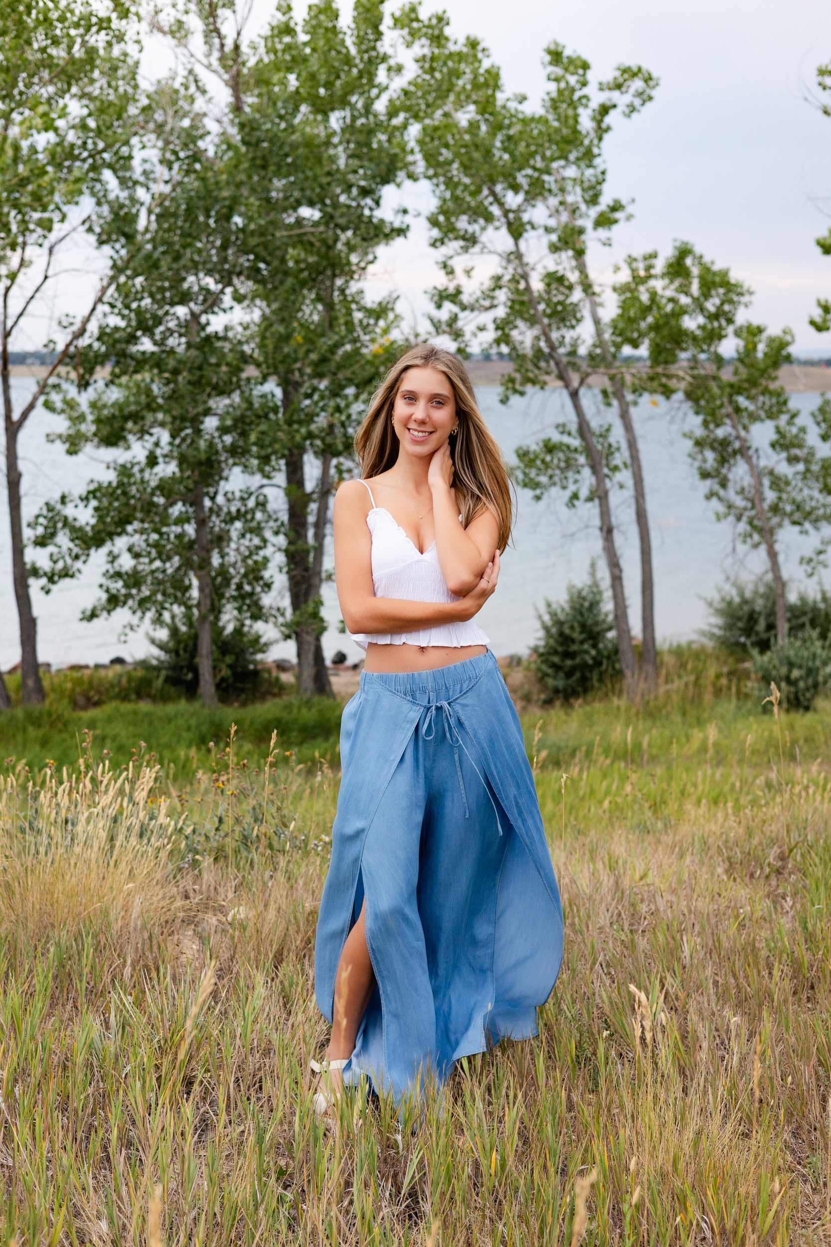 A young woman stands in a field of tall grass and smiles at the camera.
