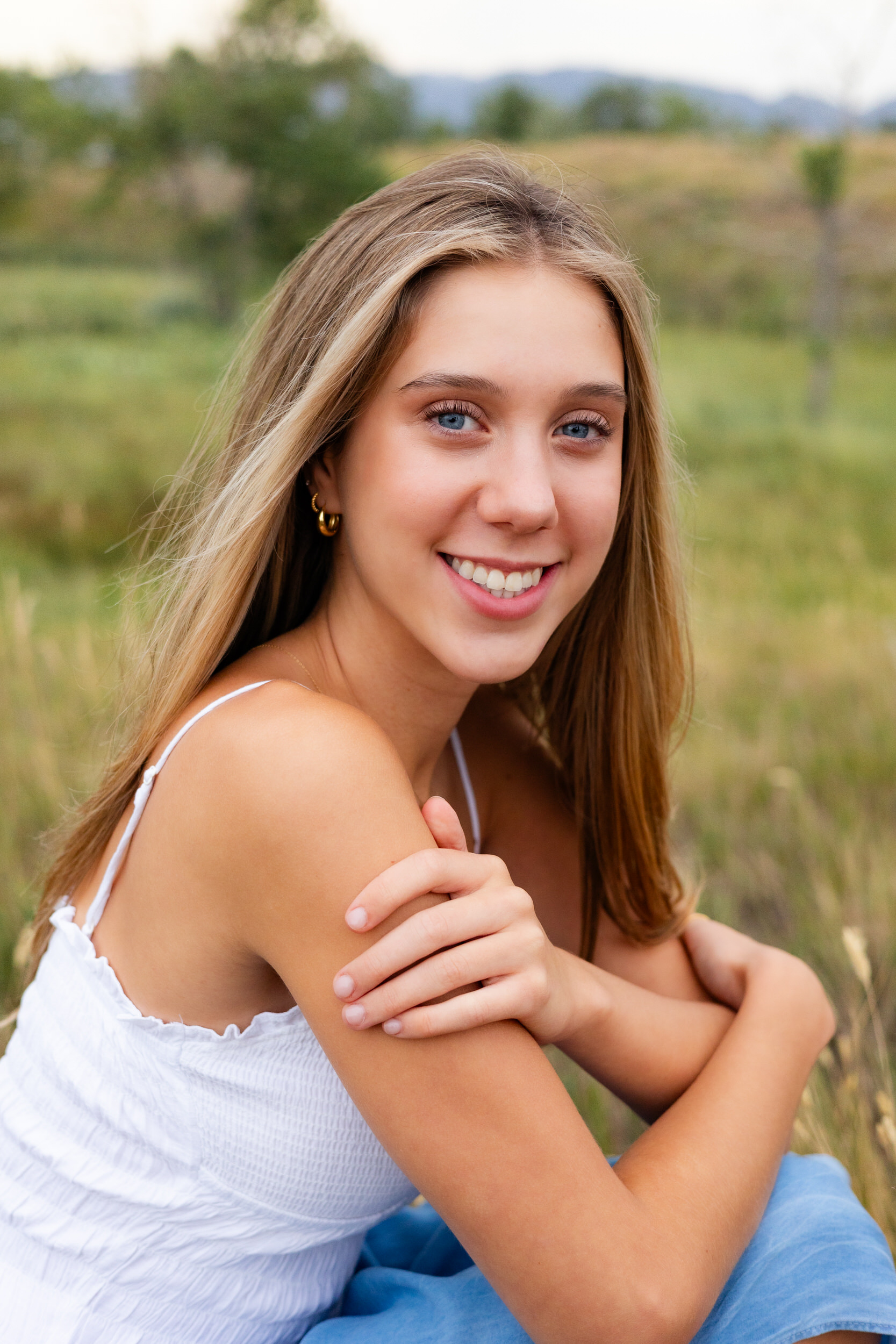A young woman sits in a field and smiles at the camera.