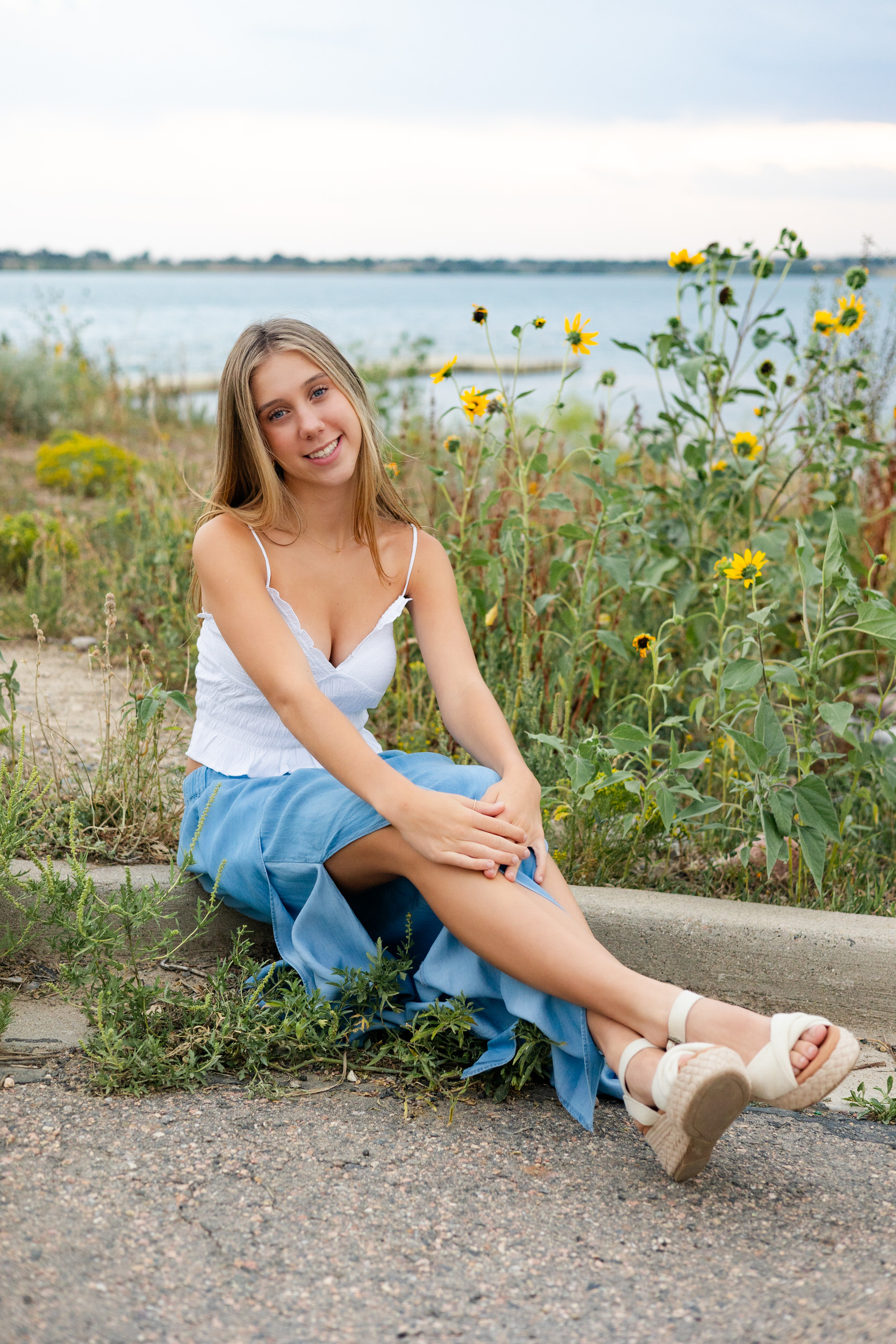 A young woman sits in front of wildflowers and smiles at the camera.