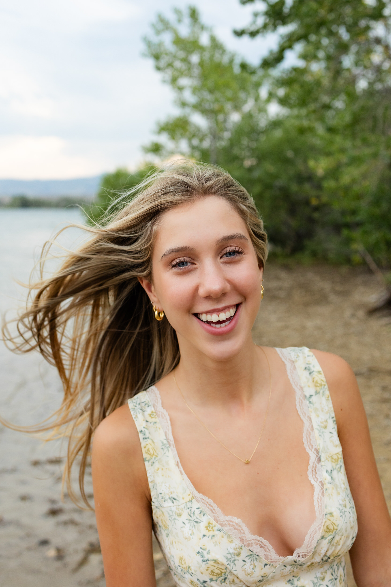 A young woman smiles at the camera as her hair blows in the wind.