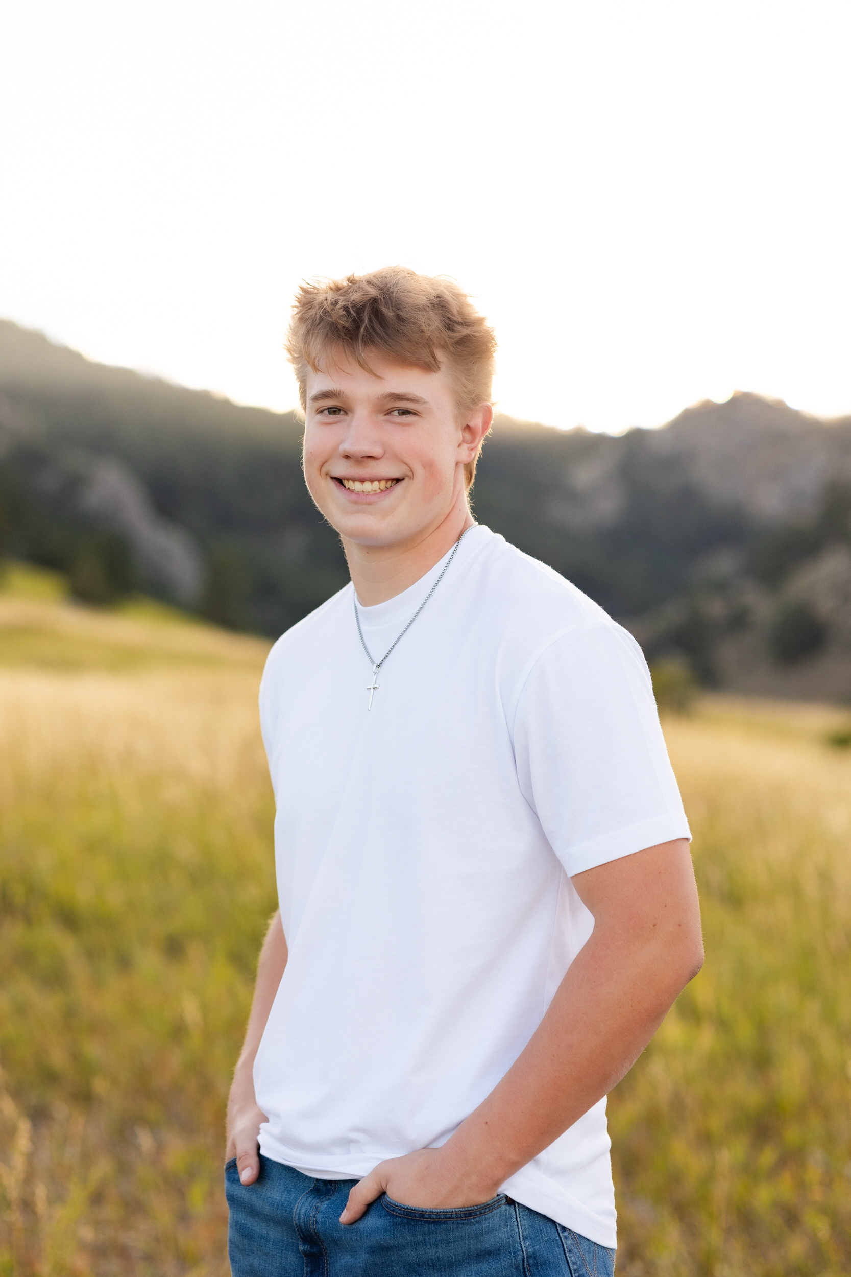 A young man stands with his hands in his pockets and smiles at the camera.