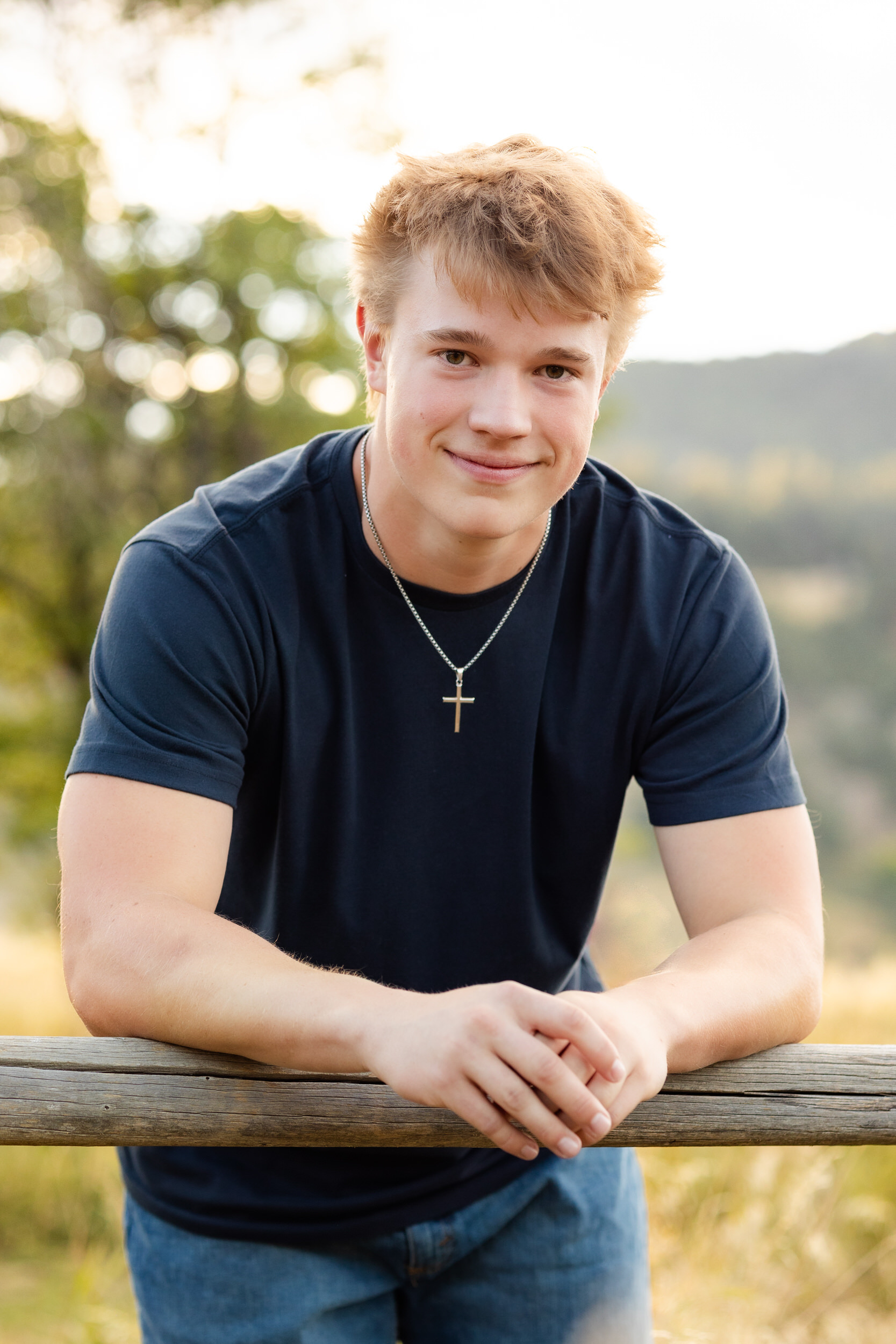 A young man leans on a fence at Chautauqua Park in Boulder, Colorado and smiles at the camera.
