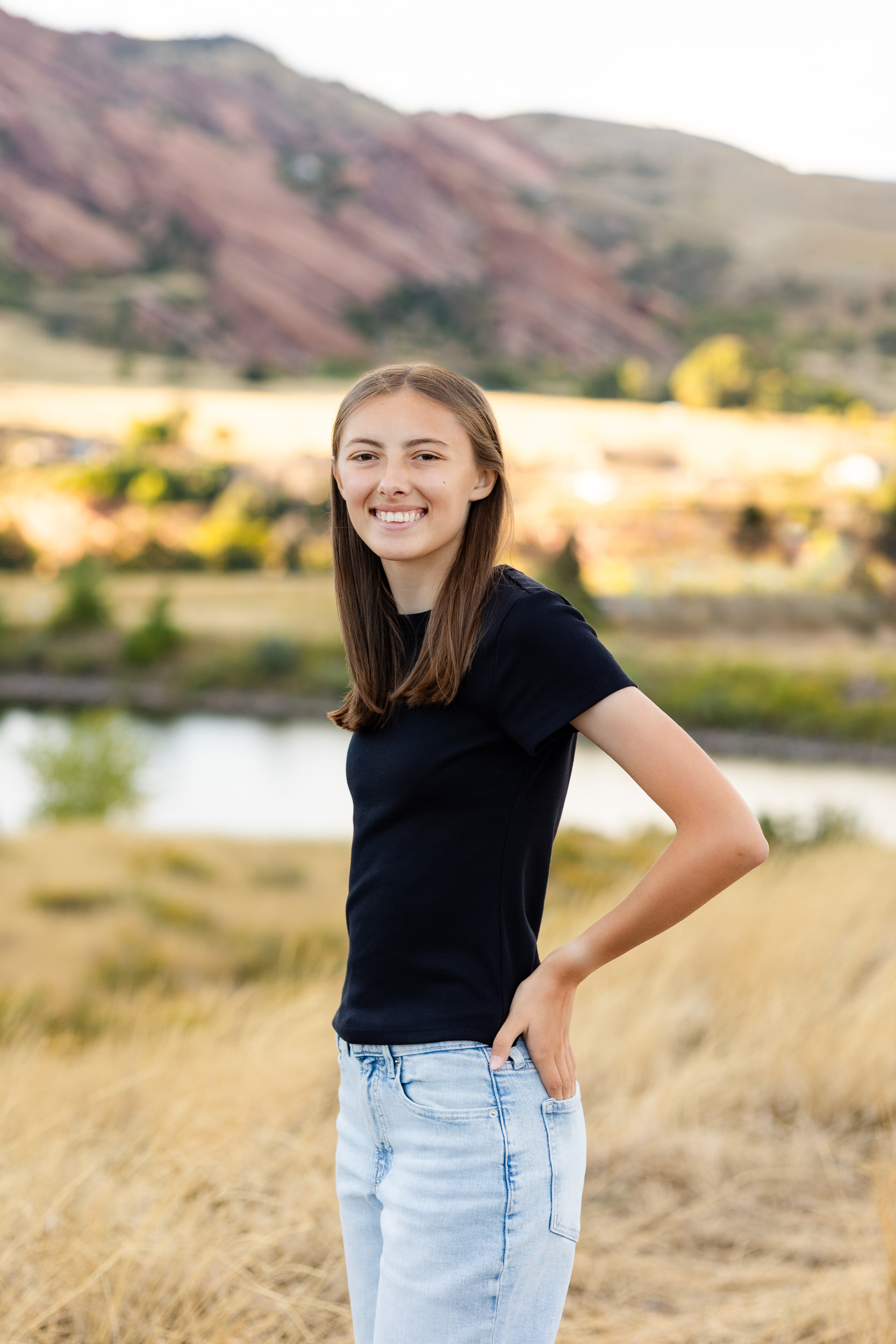 A young woman stands with her hands in her back pockets and smiles at the camera.