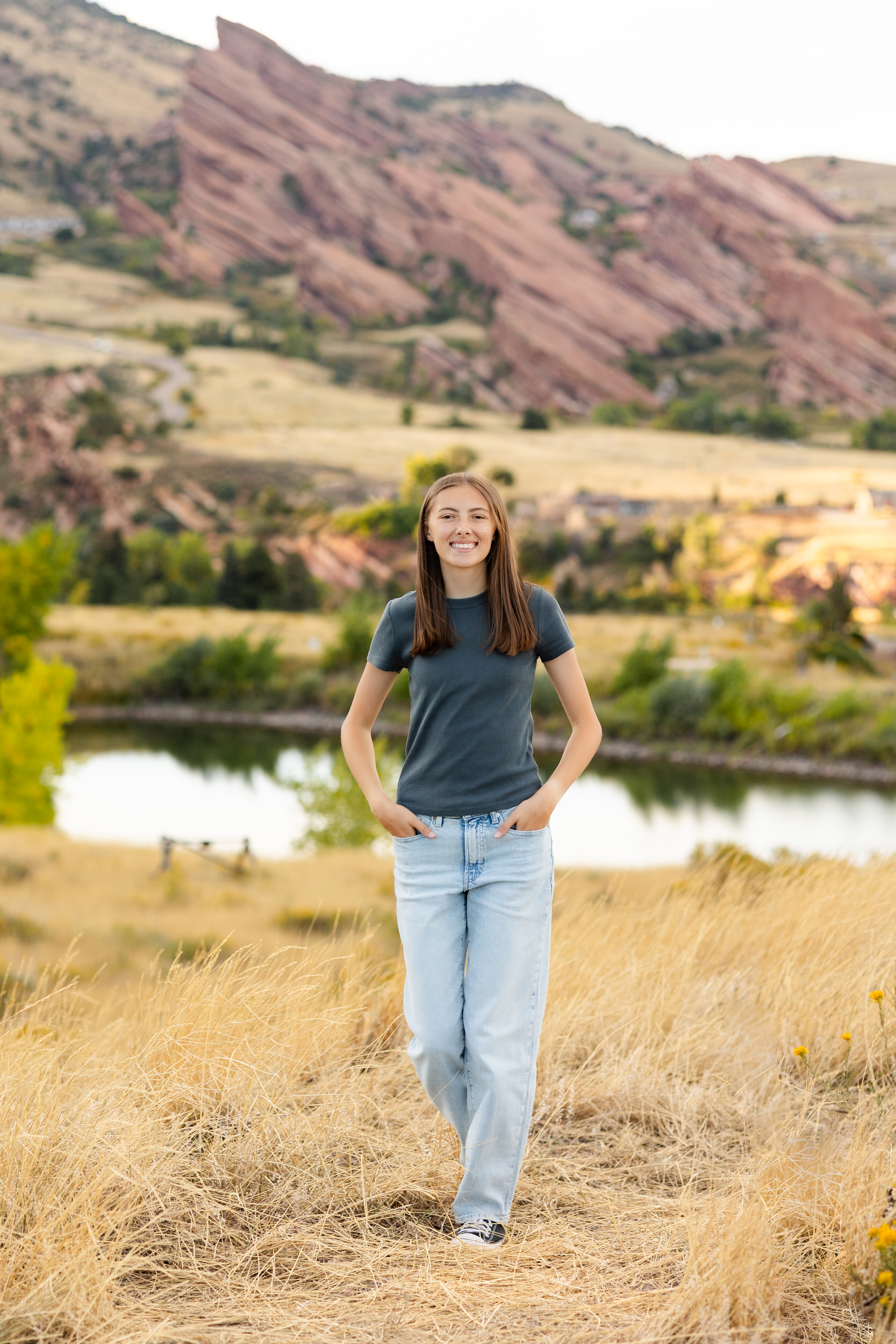 A young woman walks through a field of tall grass and smiles at the camera.