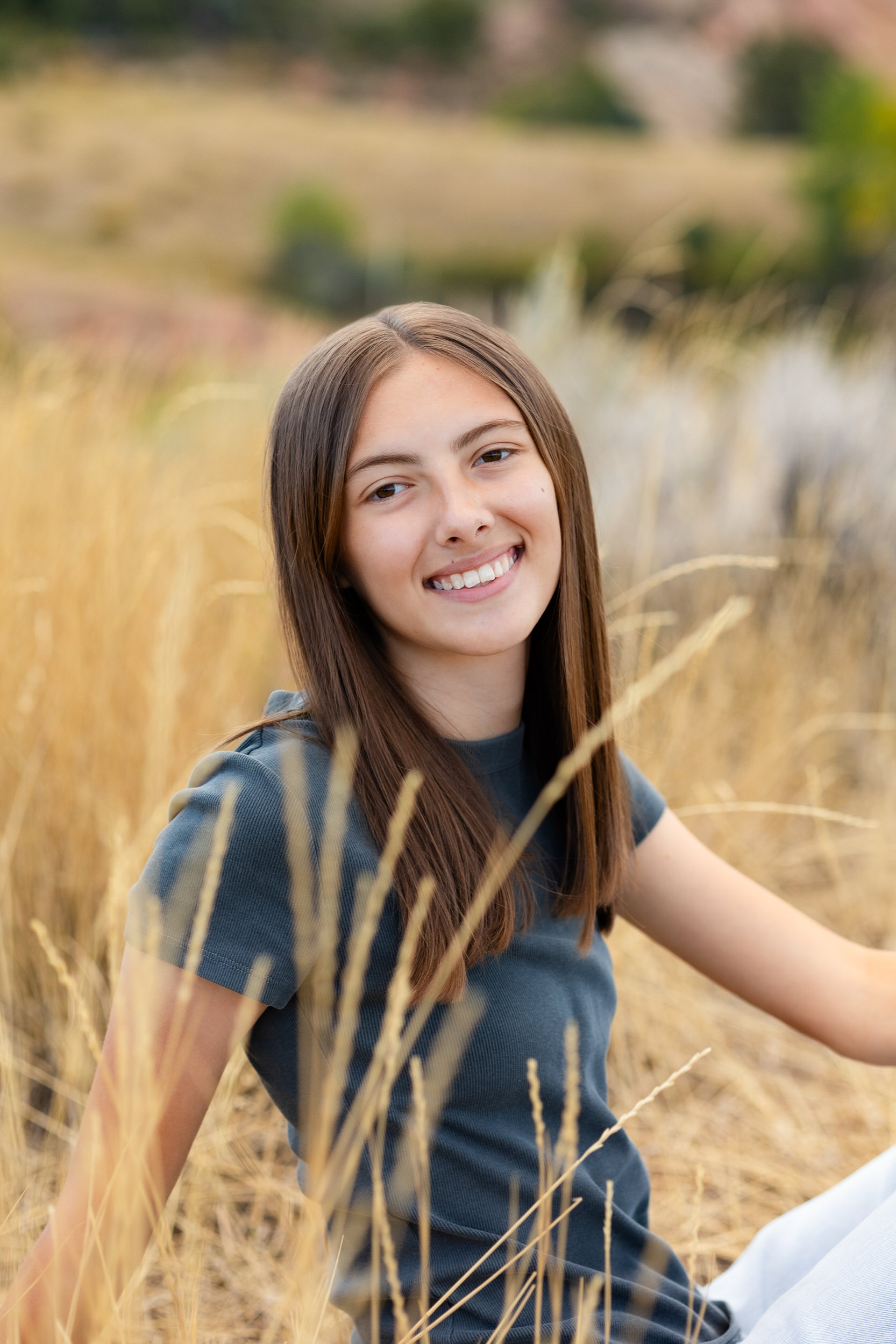 A young woman sits in a field of tall grass and smiles at the camera.