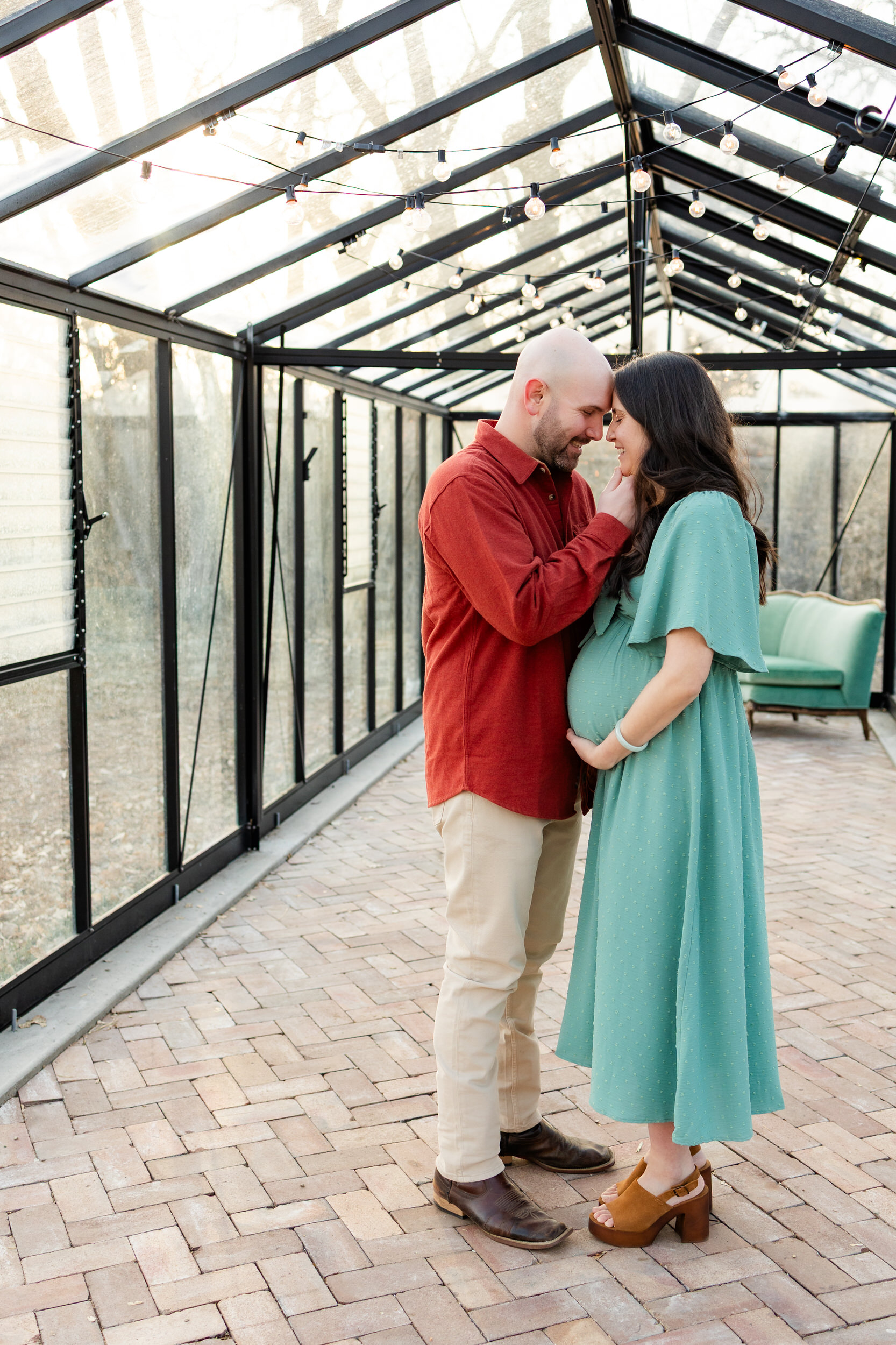 Husband and wife stand forehead to forehead smiling in a greenhouse.