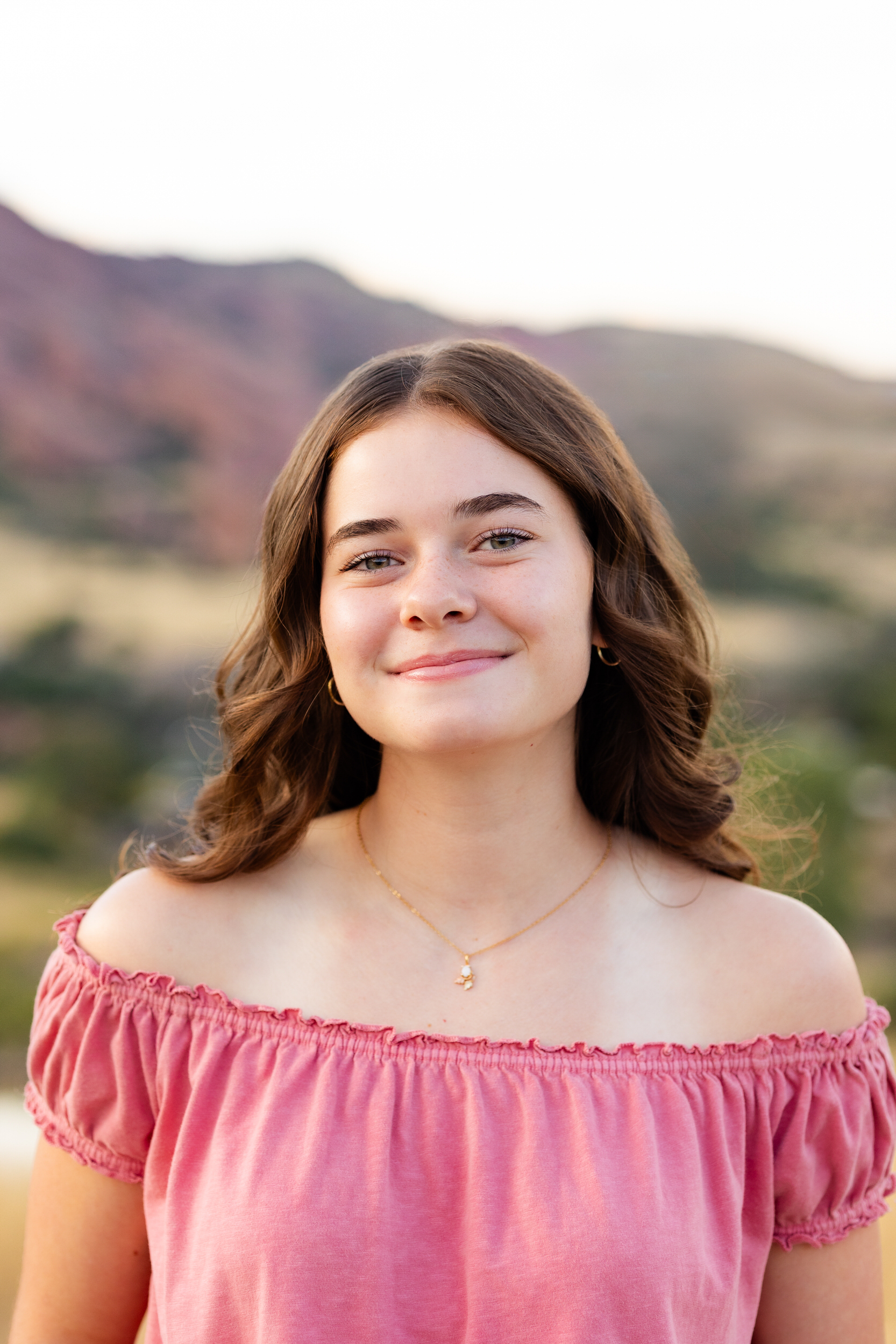 A young woman in a pink blouse smiles at the camera.