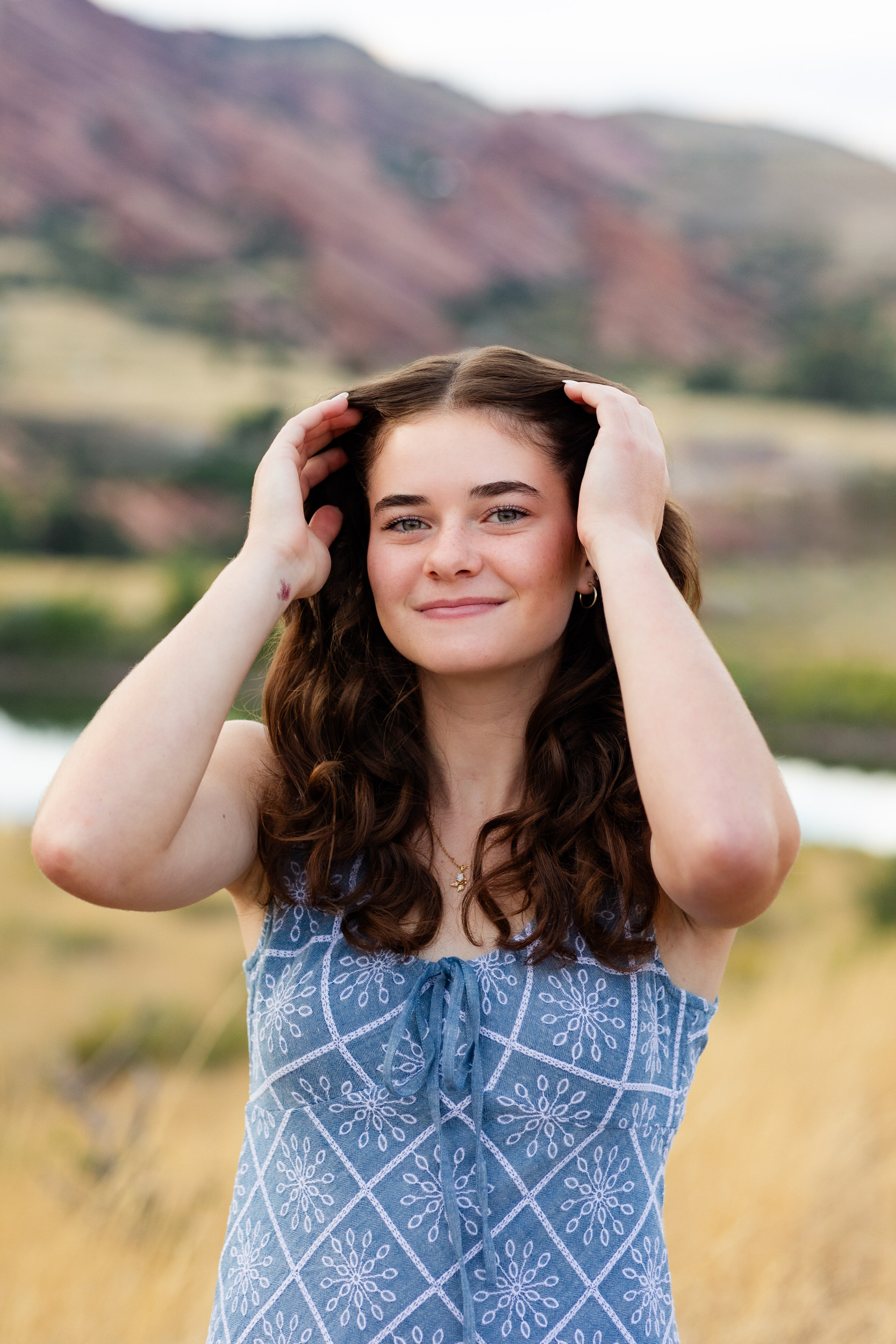 A young woman runs both hands through her hair and smiles at the camera.