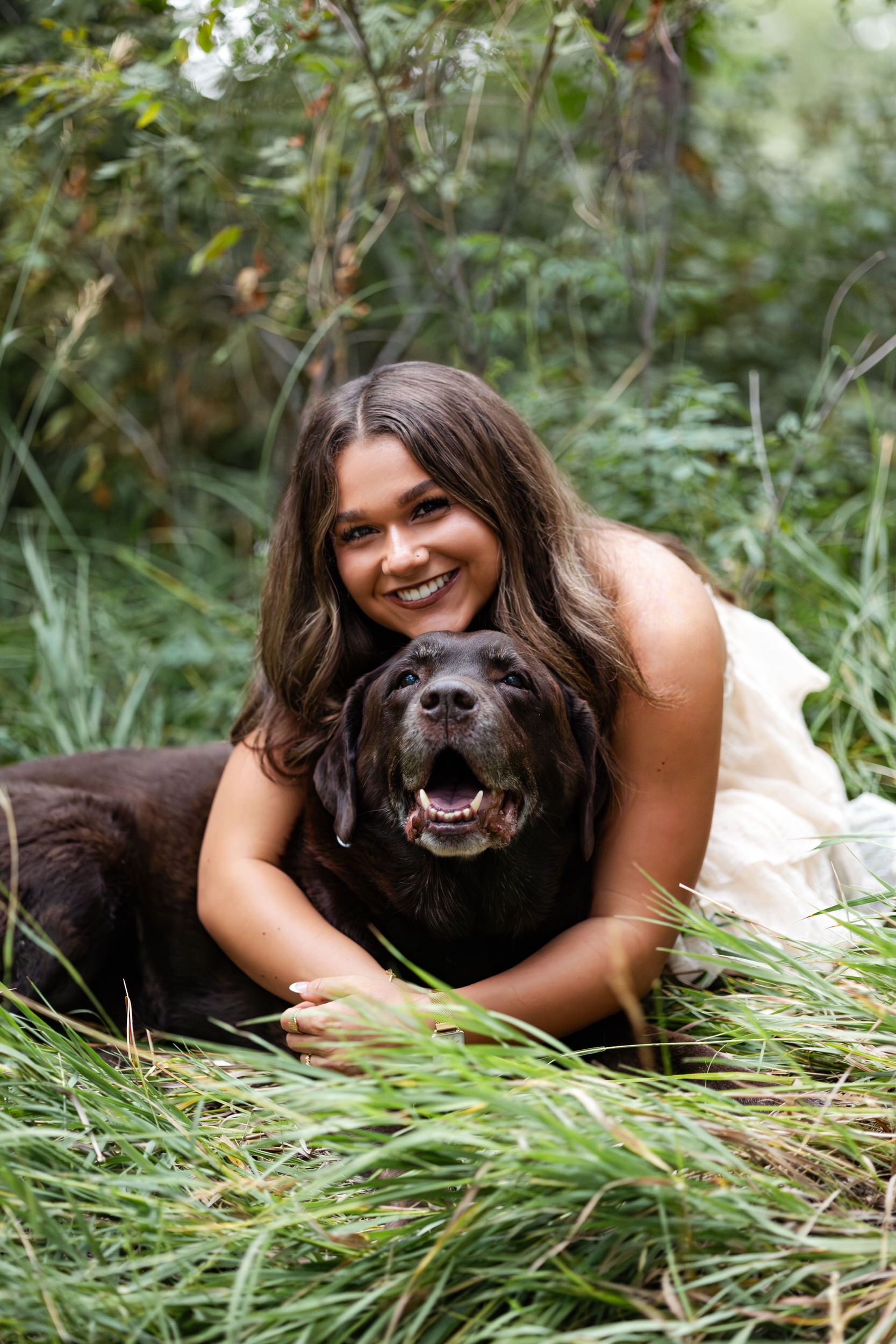 A young woman hugs her chocolate Labrador and smiles at the camera.