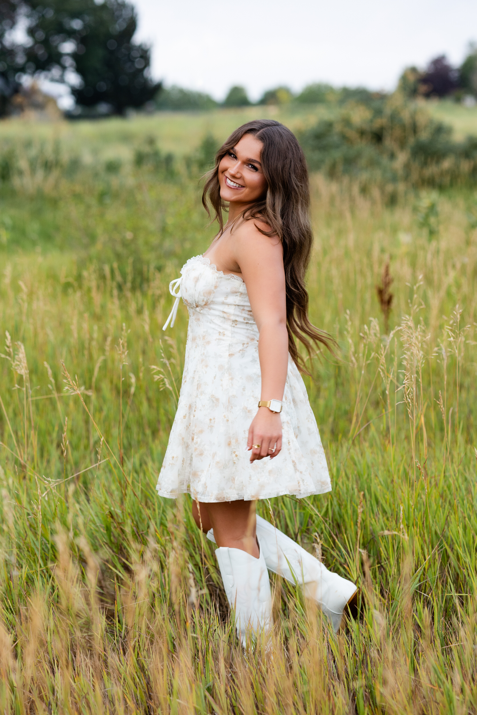 A young woman walks through a field of tall grass and smiles at the camera.