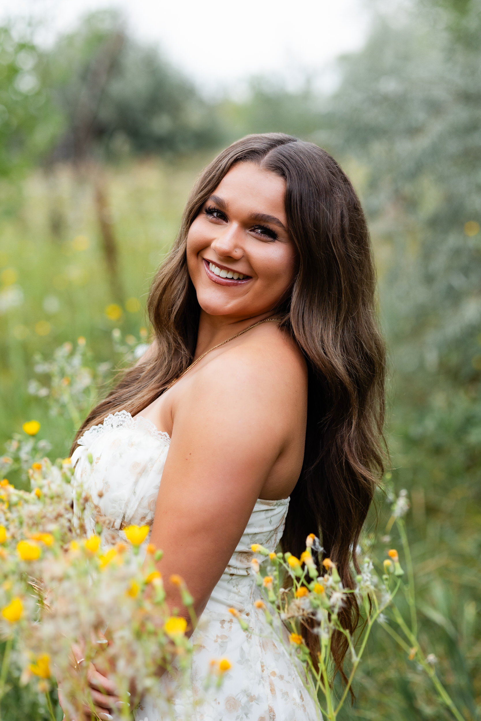 A young woman stands among yellow wild flowers and smiles at the camera.
