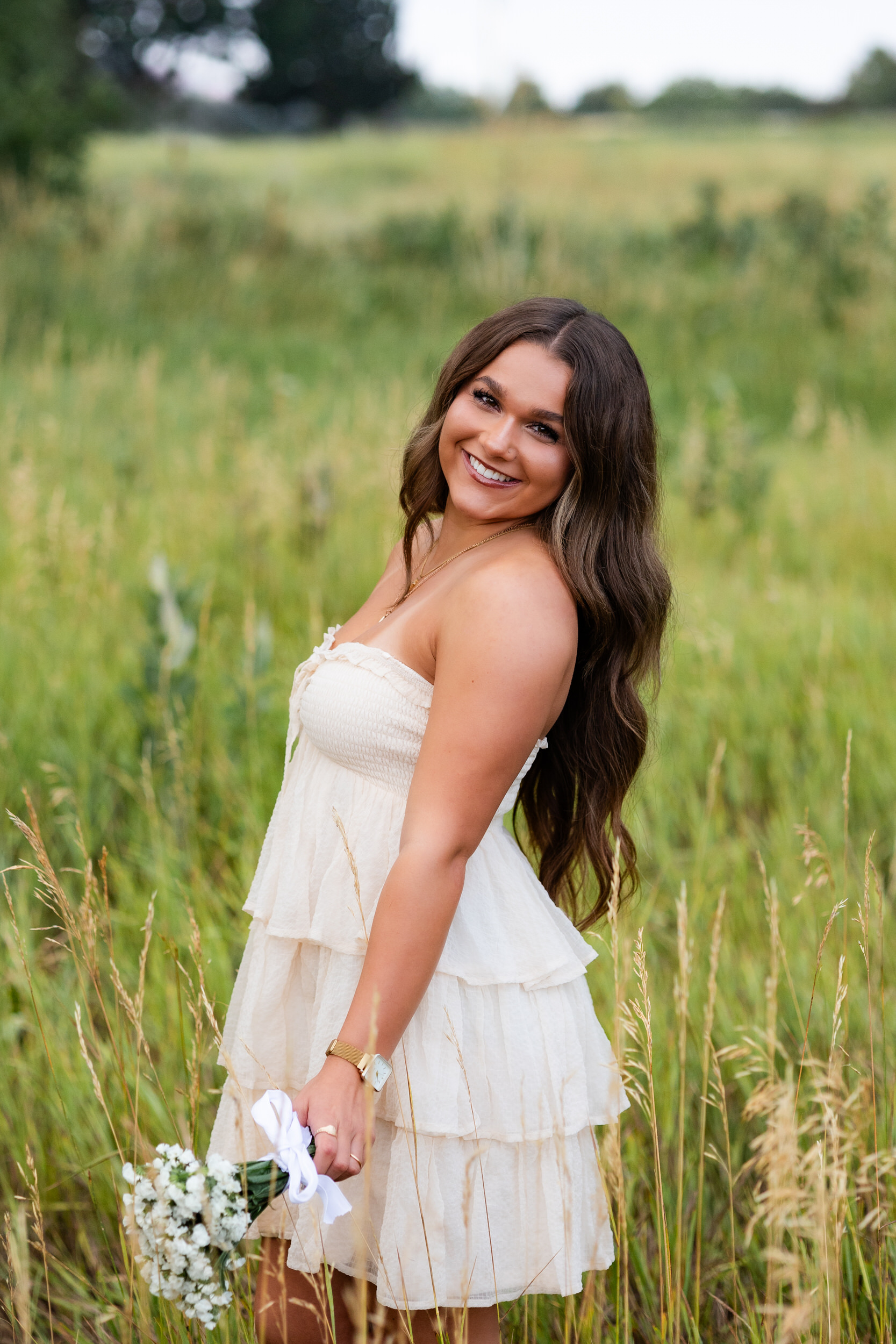 A young woman holding a bouquet of baby's breath looks over her shoulder and smiles at the camera.