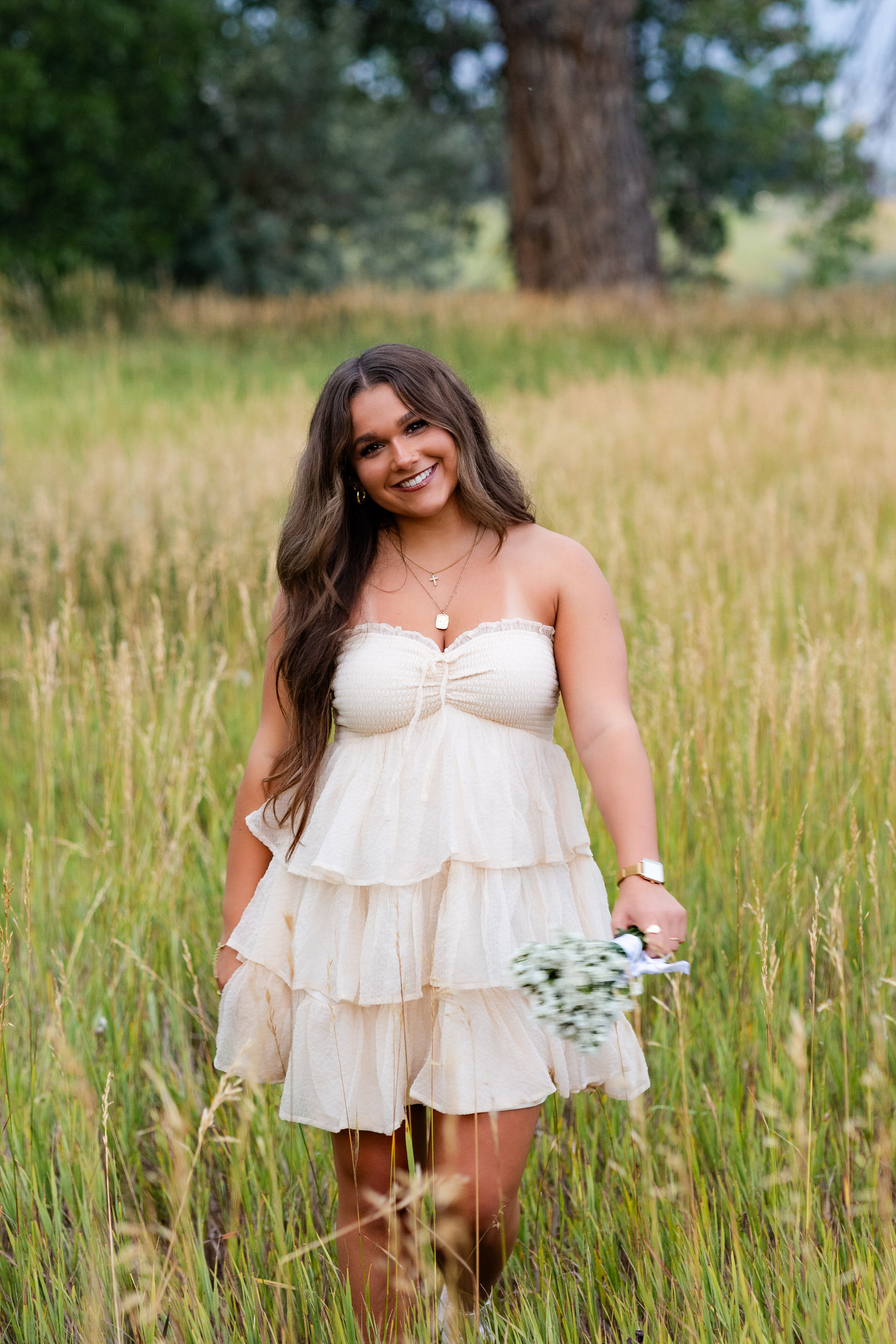 A young woman walks through a field of tall grass and smiles at the camera.