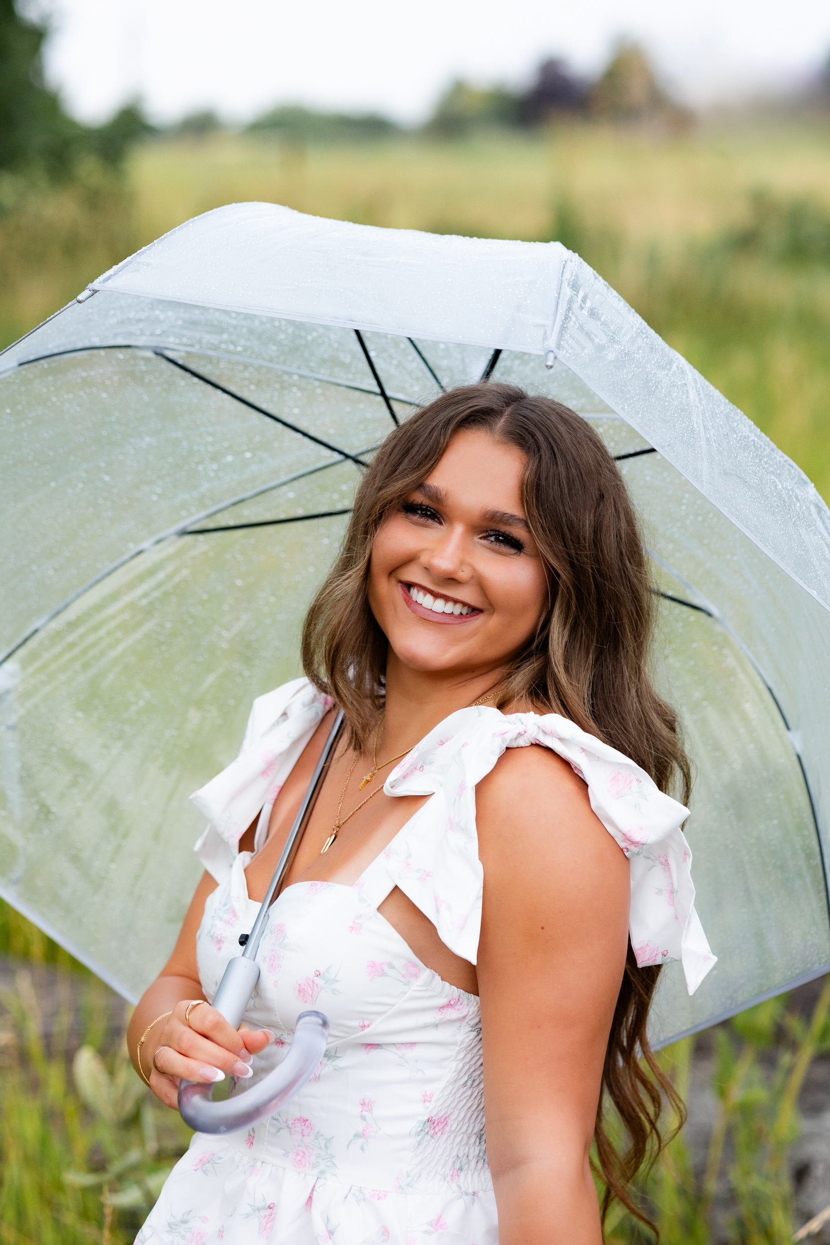 A young woman holding an umbrella smiles at the camera.