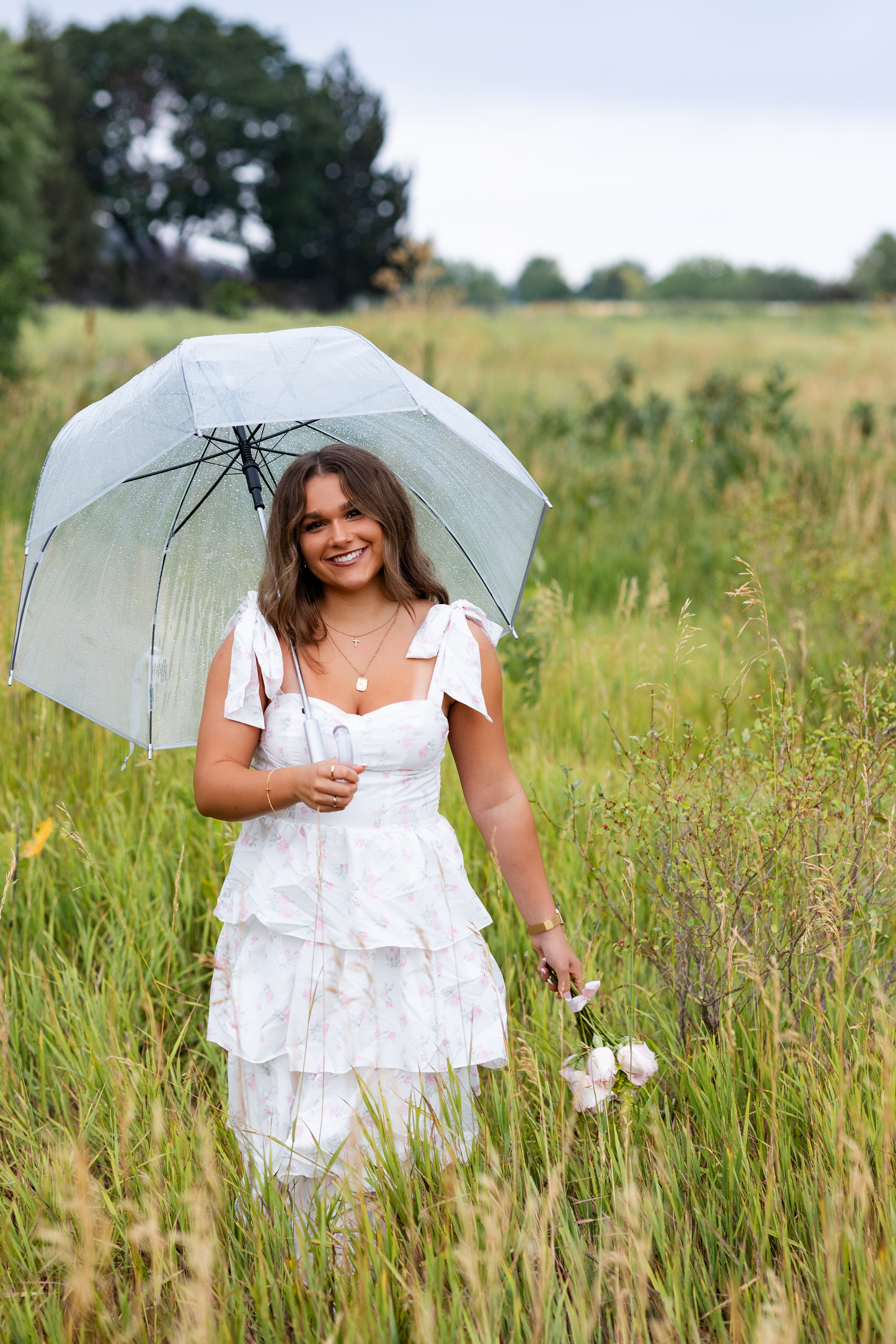 A young woman holding an umbrella and a bouquet of roses smiles at the camera.