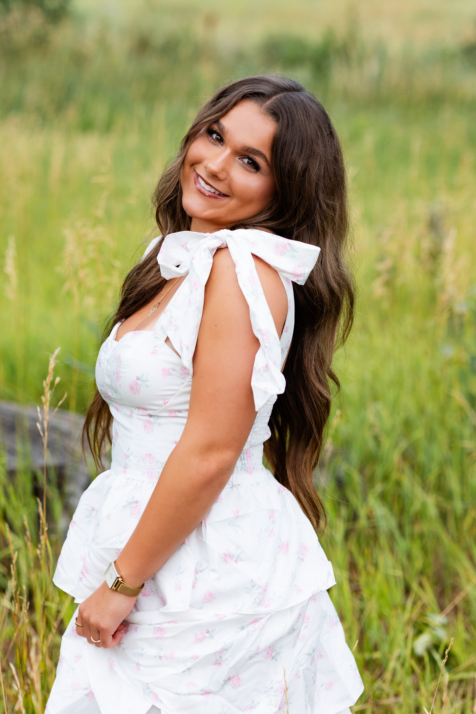 A young woman in a white dress looks over her shoulder and smiles at the camera.