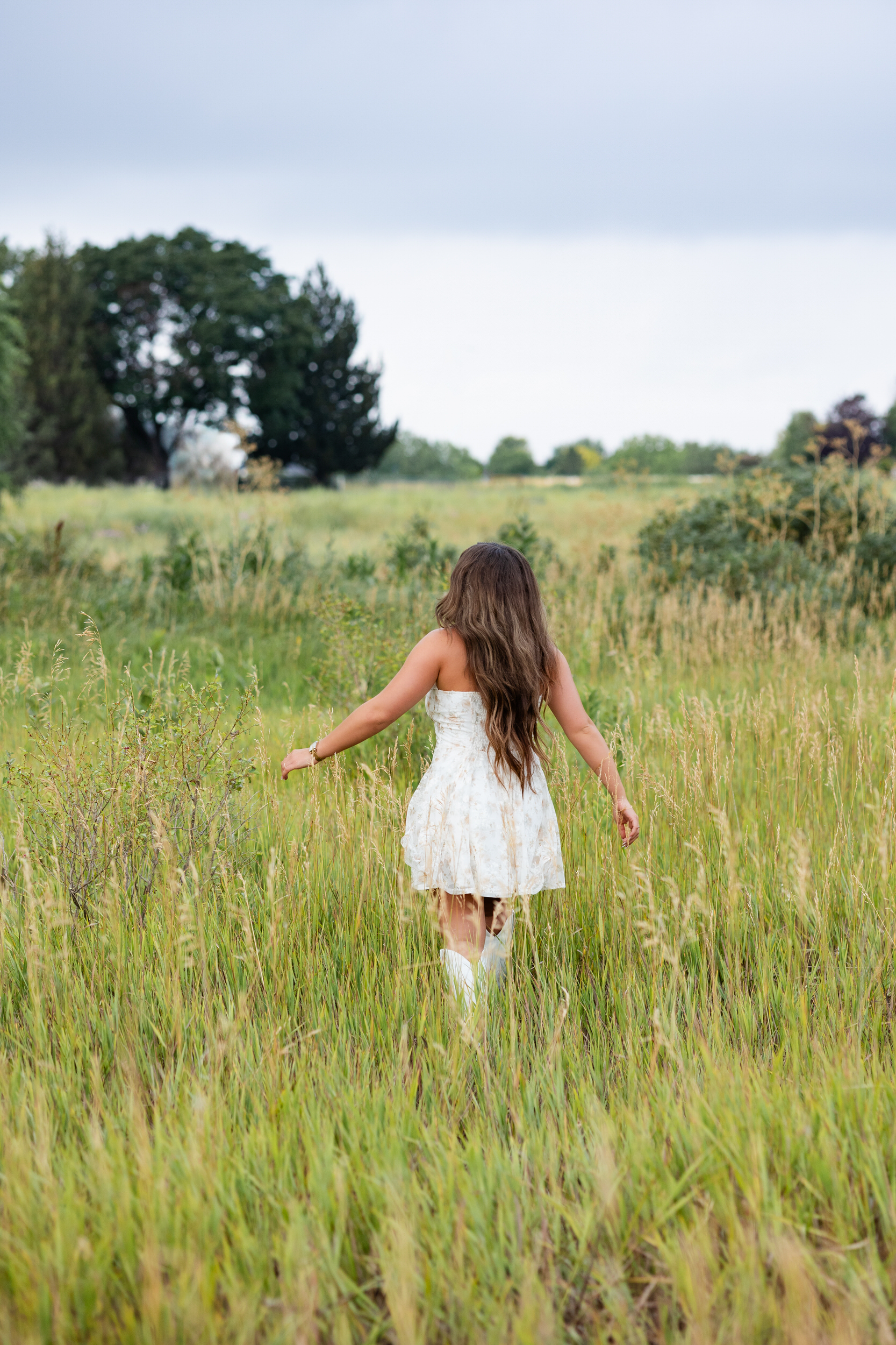 A young woman walks away from the camera in a field of tall grass.