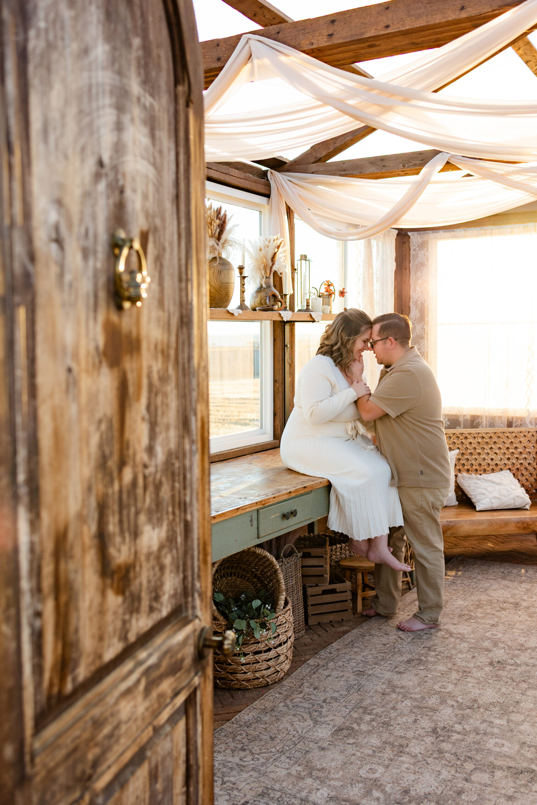 Husband and wife lean forehead-to-forehead in a greenhouse.