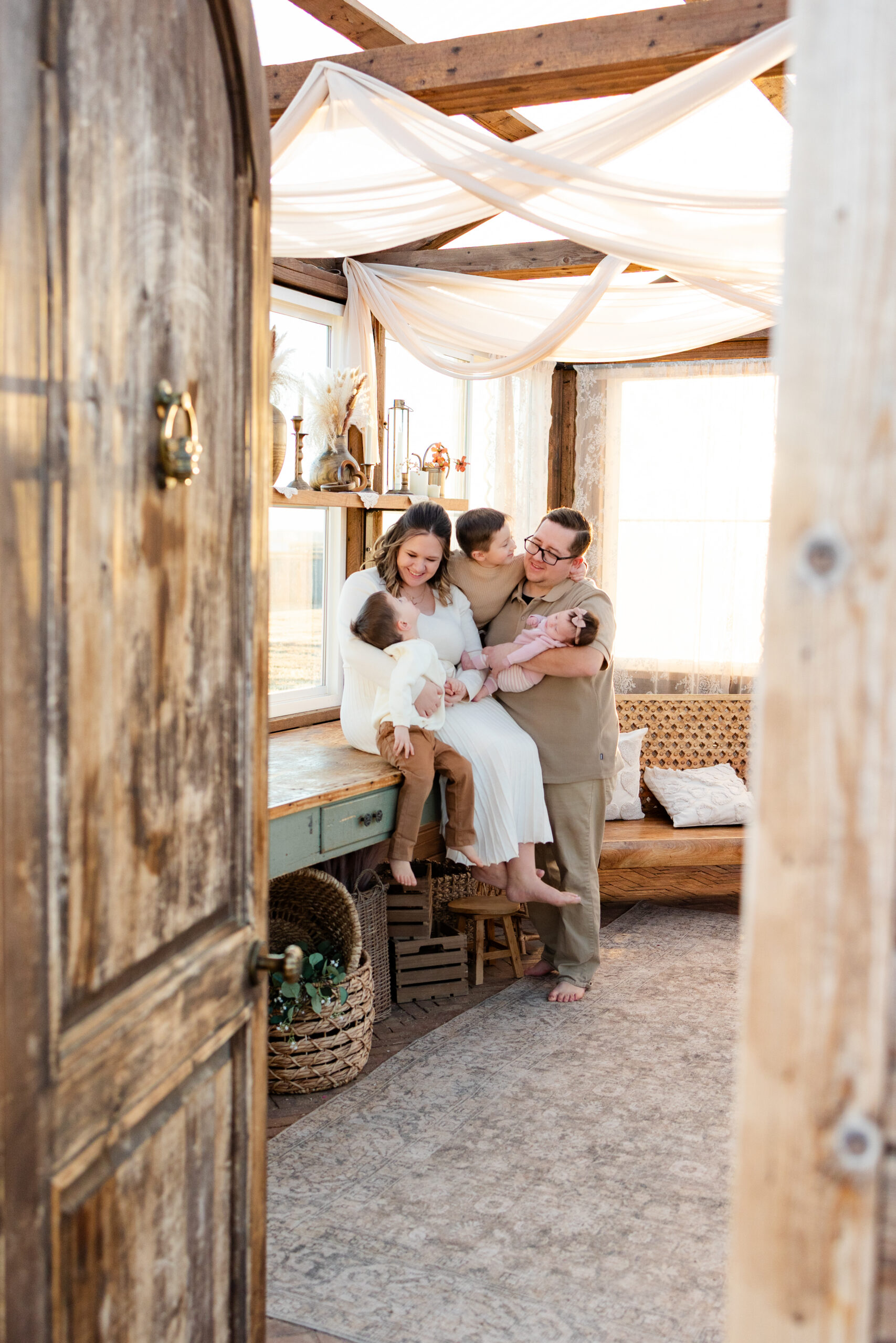 A family of five looks and smiles at each other in a greenhouse.