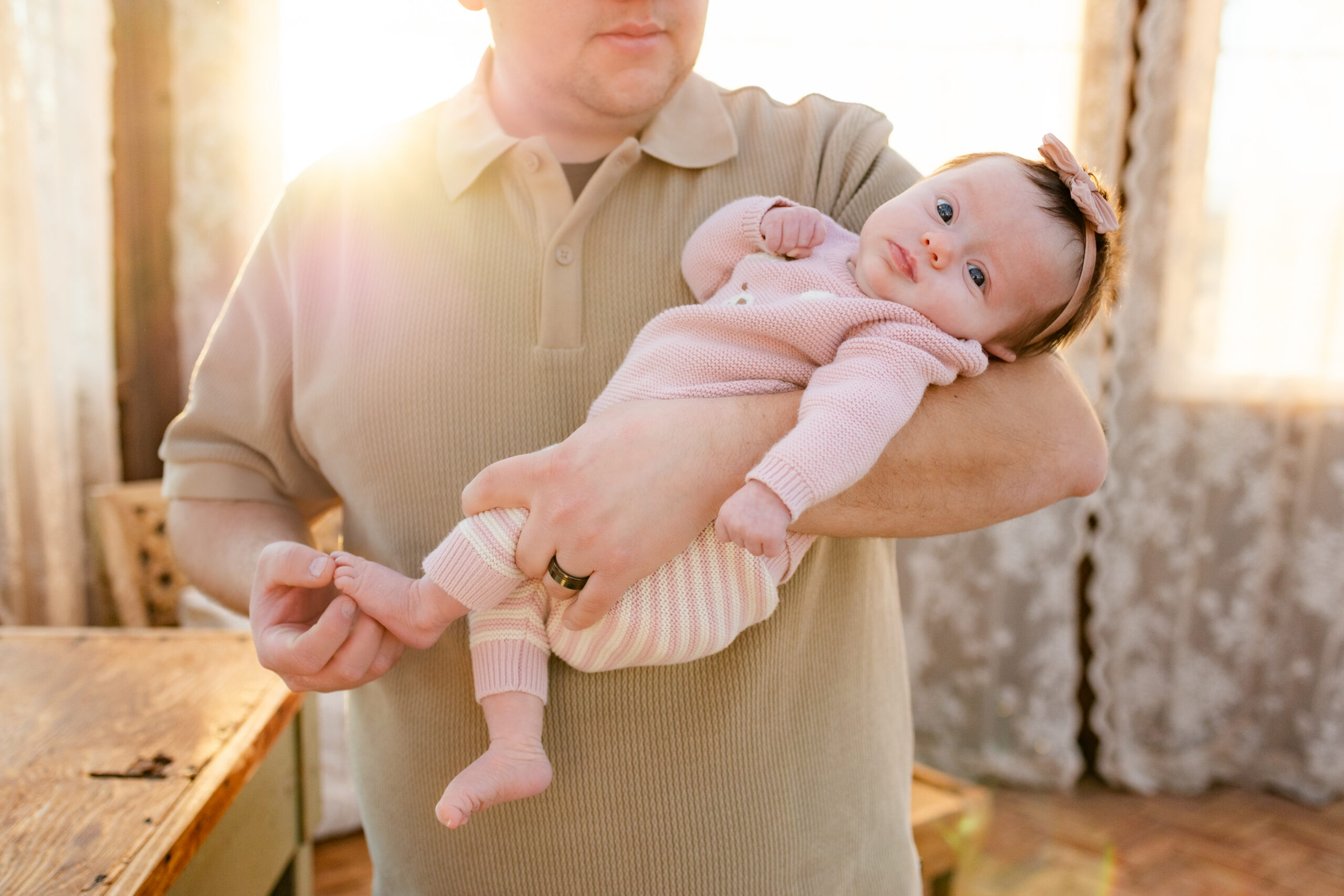 Dad holds newborn daughter as she looks at the camera.