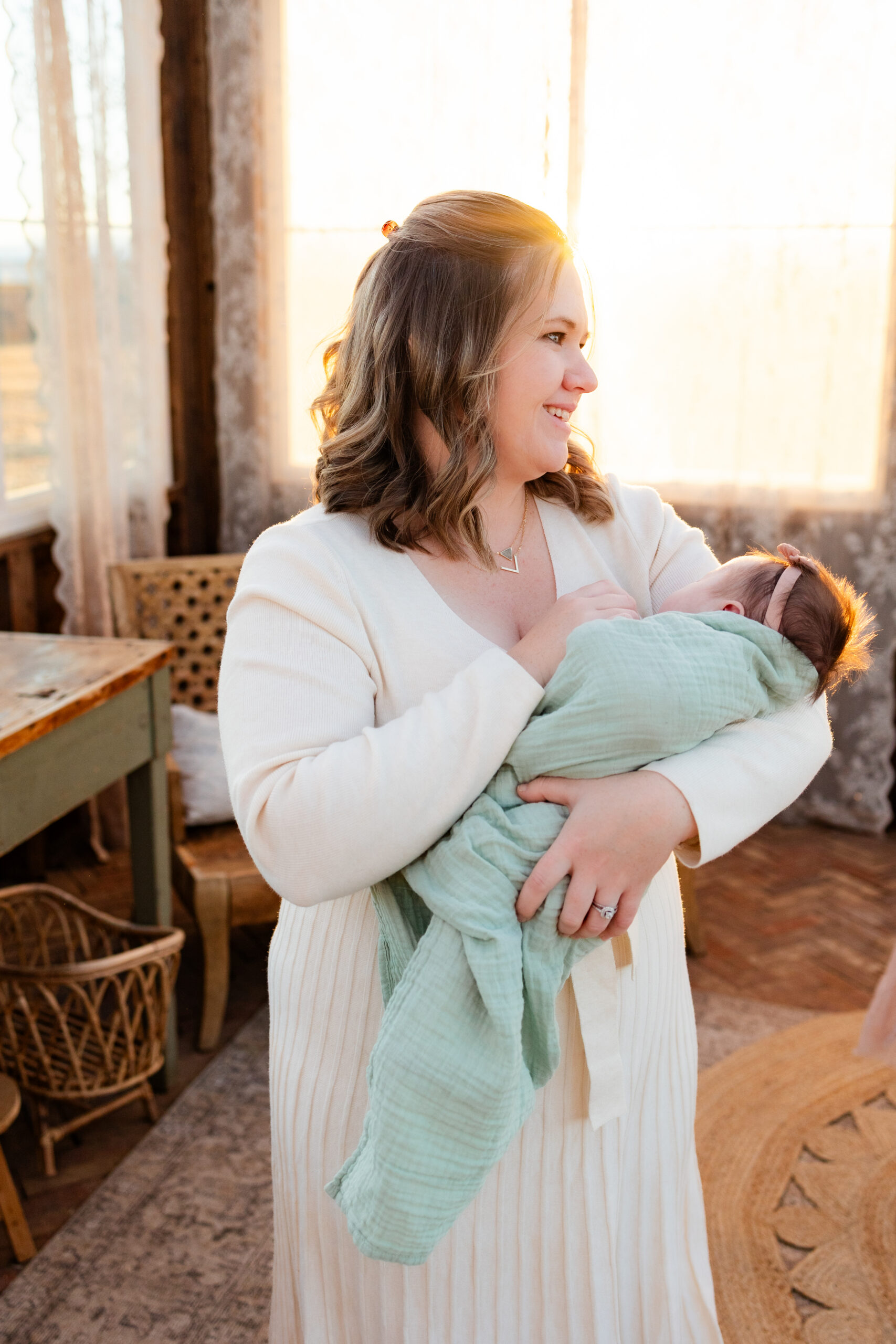 Mom holds newborn daughter and smiles over her shoulder off-camera.