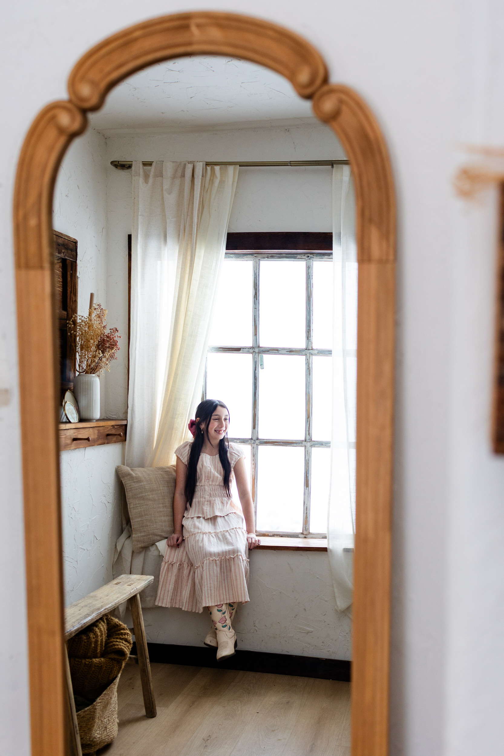 Photo of a mirror with a reflection of a girl sitting in a windowsill.