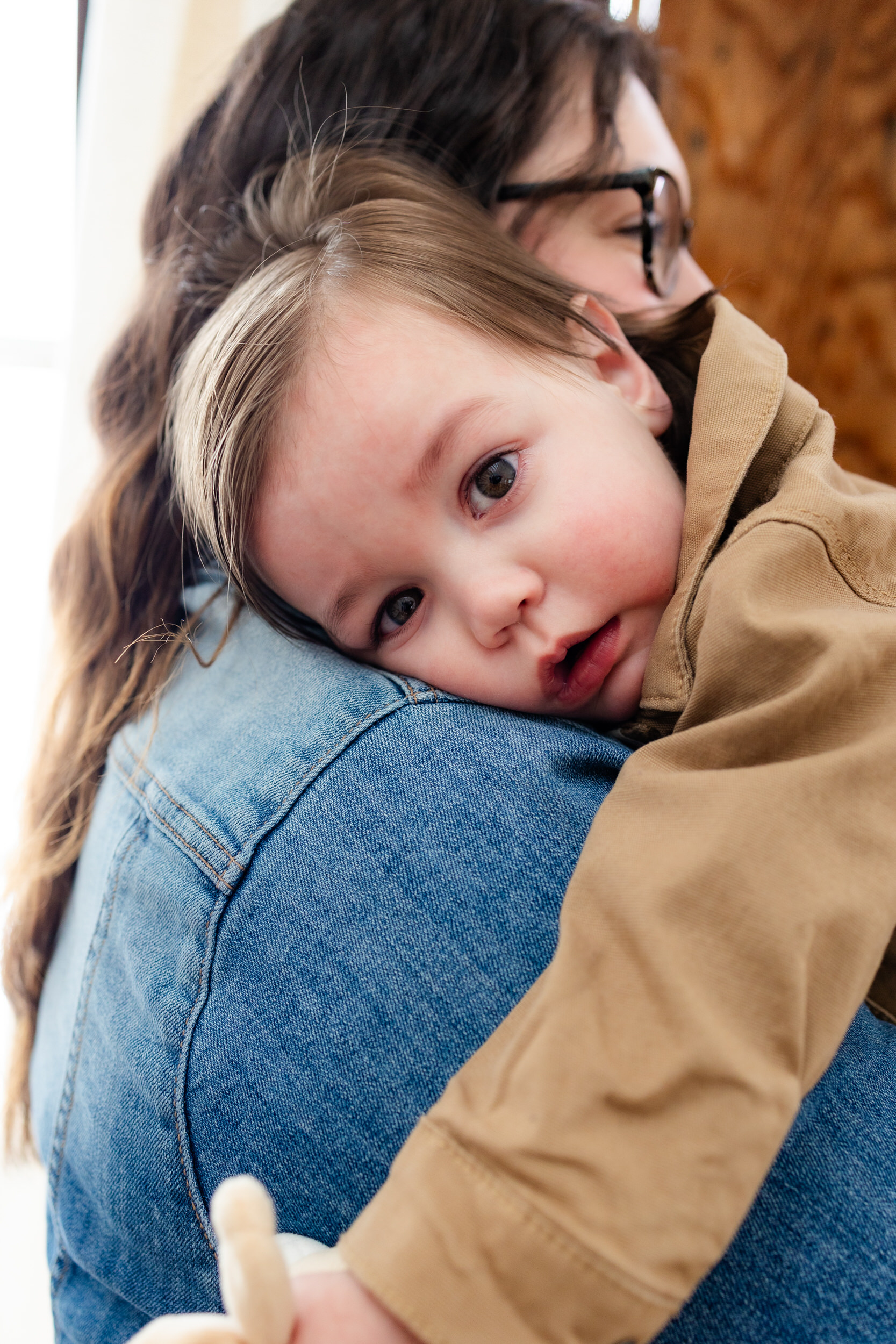 One-year-old-boy rests his head on his mom's shoulder.