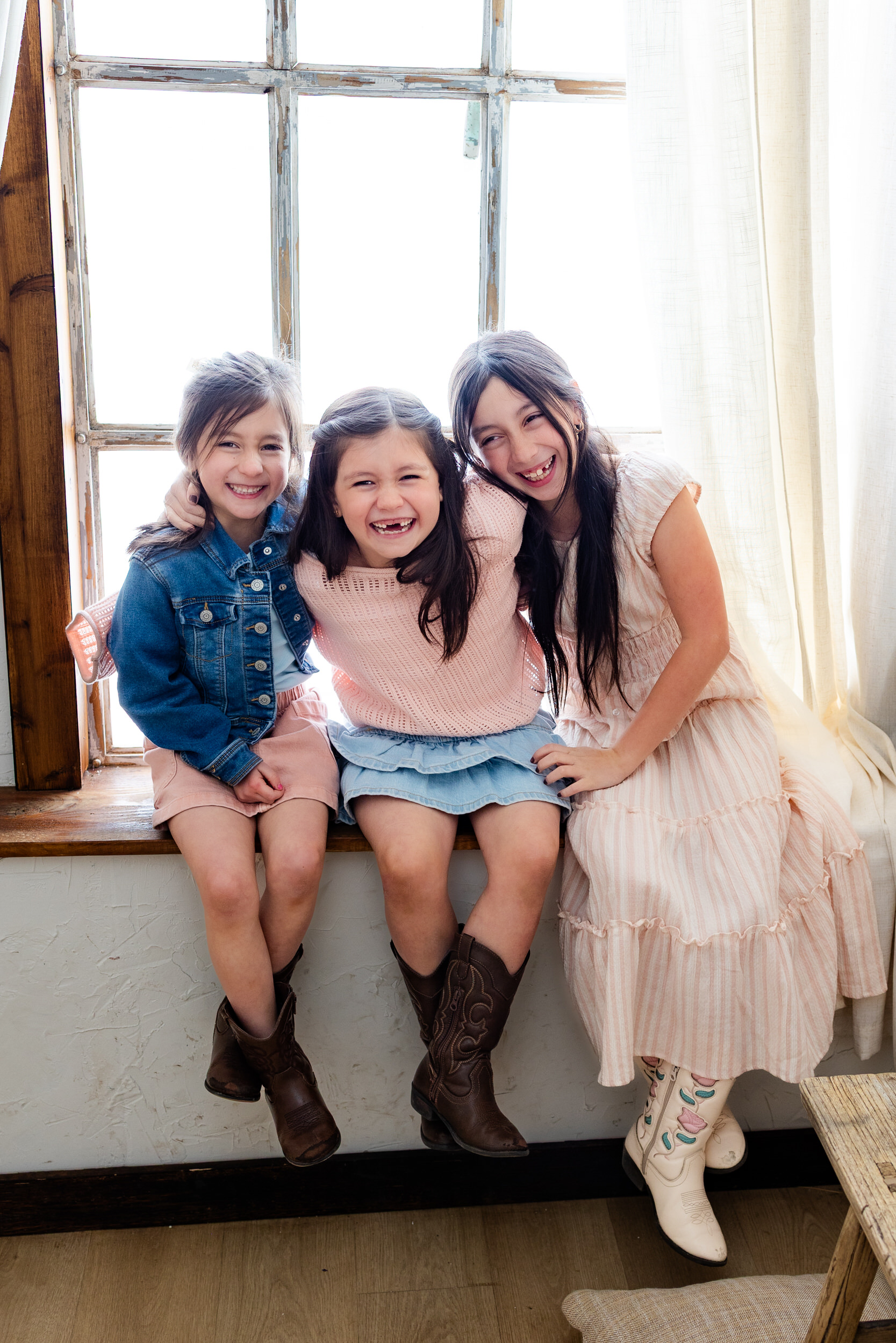 Three sisters sit in a windowsill and laugh together.