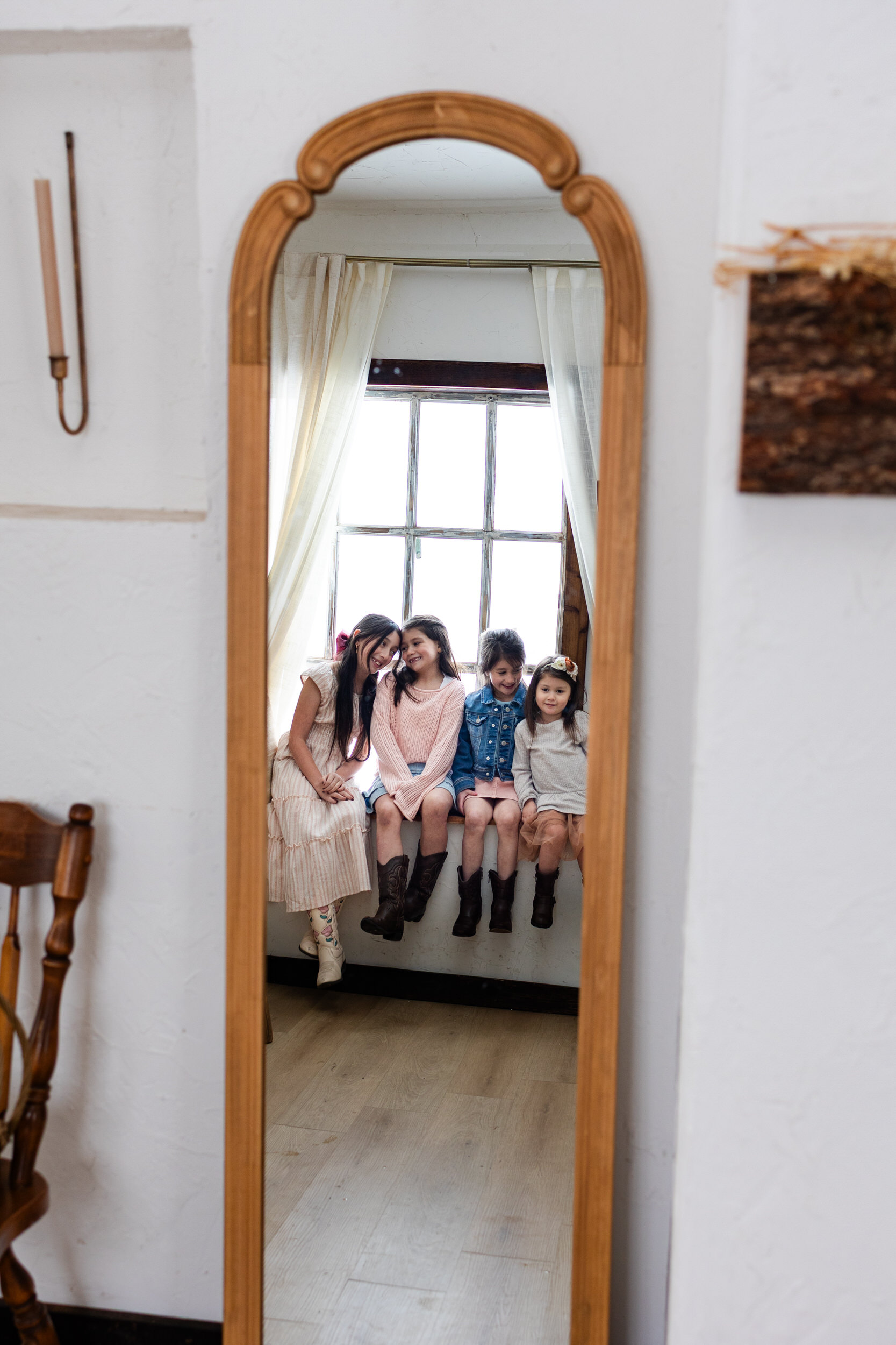 Photo of a mirror with a reflection of four sisters sitting in a windowsill and smiling at each other.