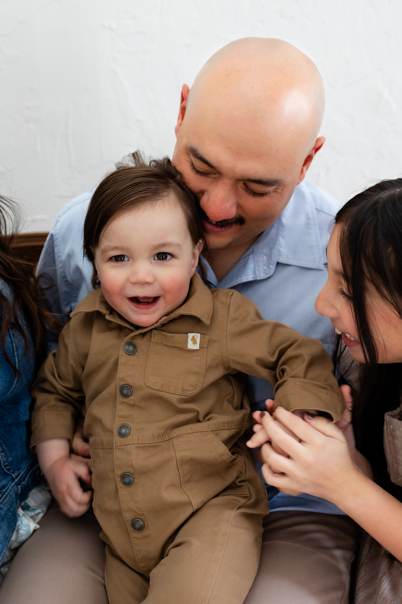 A one-year-old boy sits in his dad's lap and smiles at the camera.