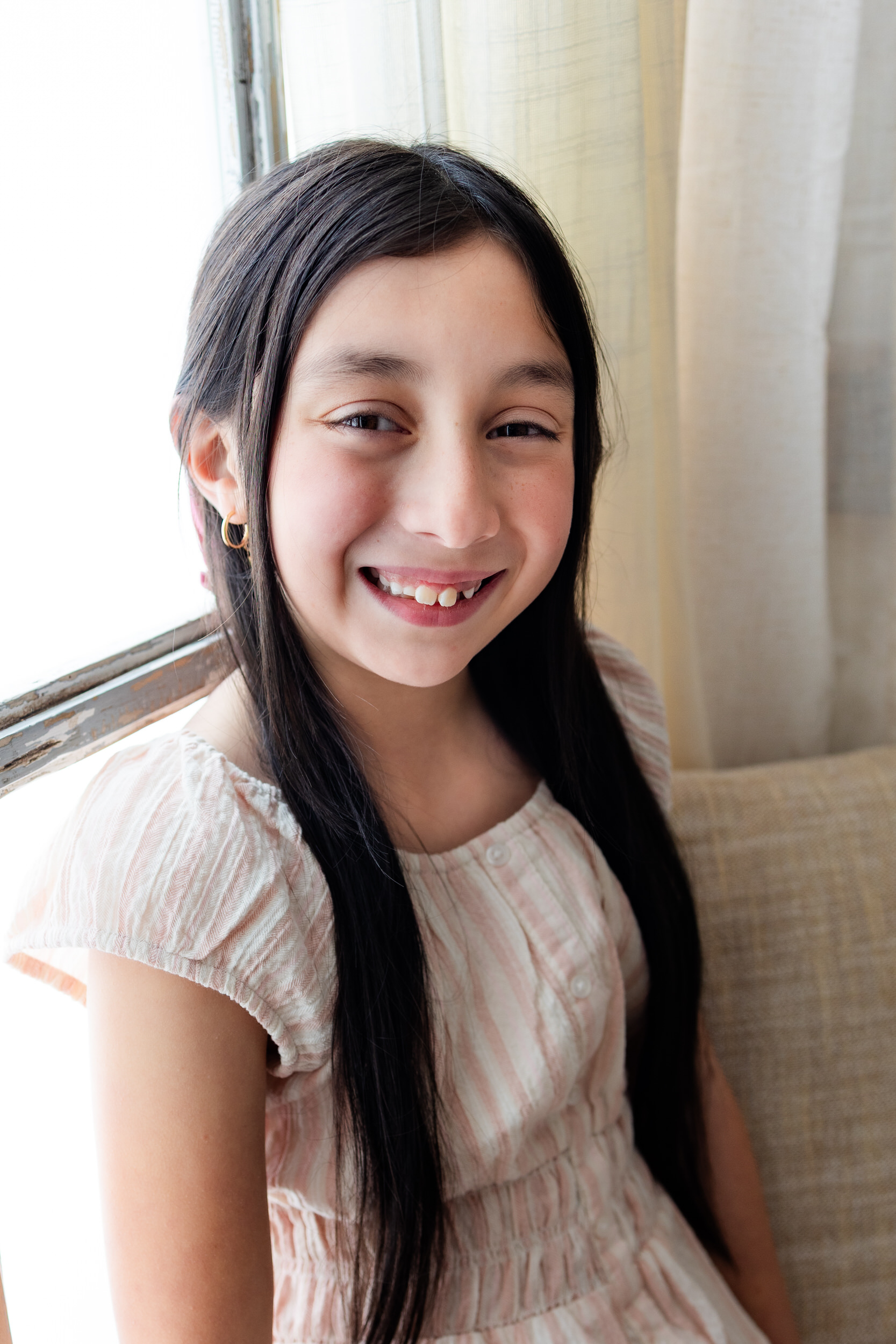 A young girl sits in a windowsill and smiles at the camera.