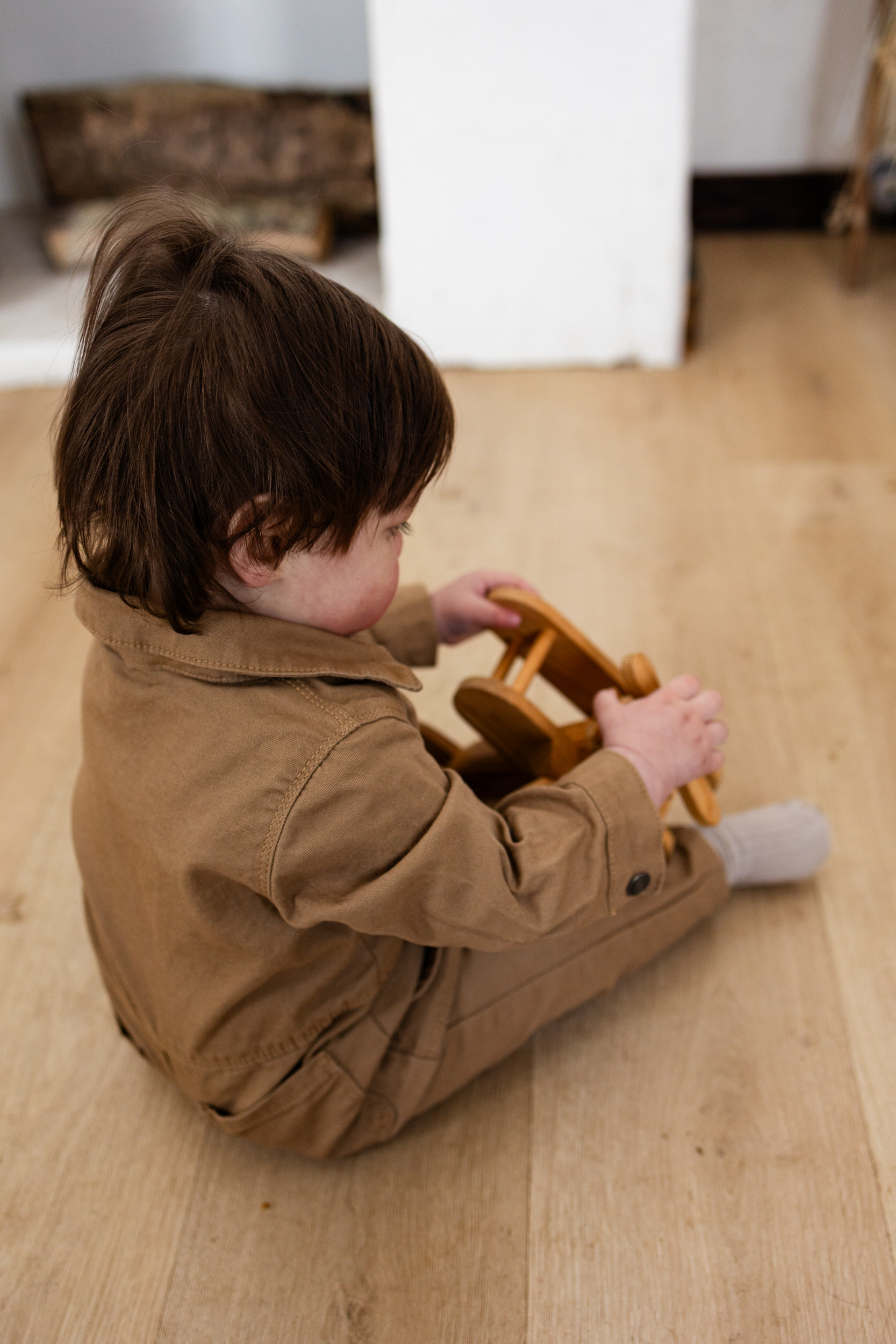 A little boy sits on the floor playing with a wooden plane.