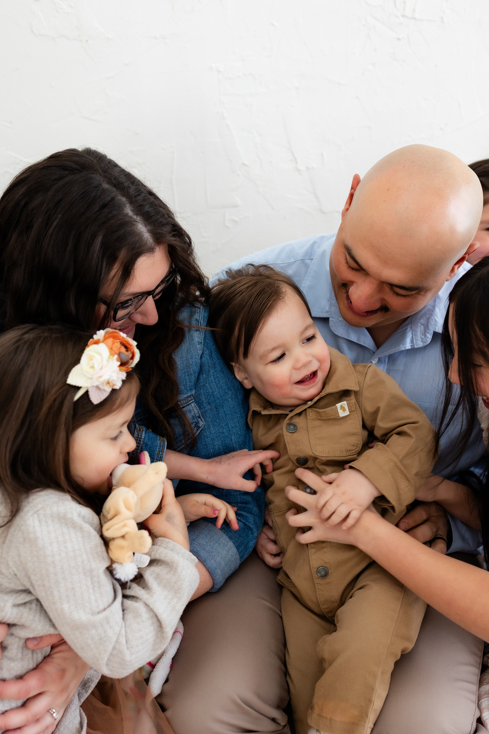 Mom, dad, and sisters dote on one-year-old boy sitting in dad's lap.