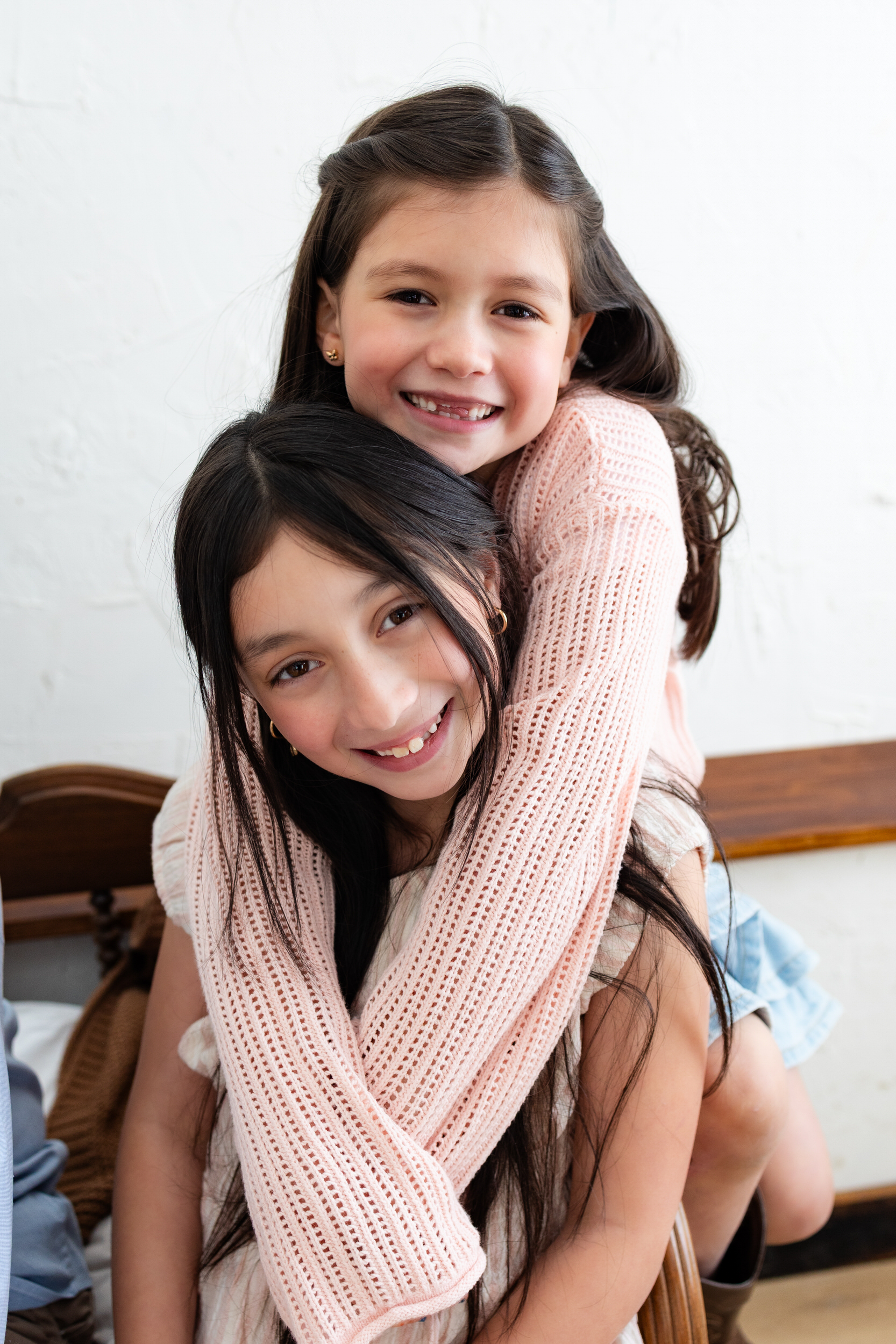 Two sisters hug each other and smile at the camera.