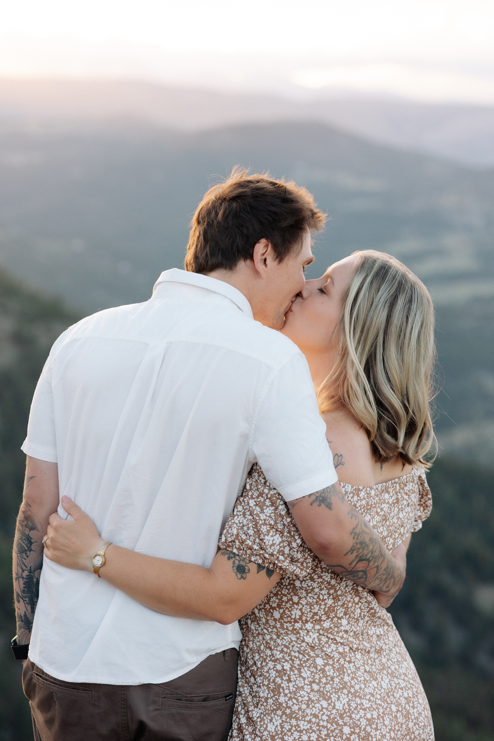 Husband and wife share a kiss with a sweeping mountain view behind them at Lost Gulch Overlook in Boulder, Colorado.