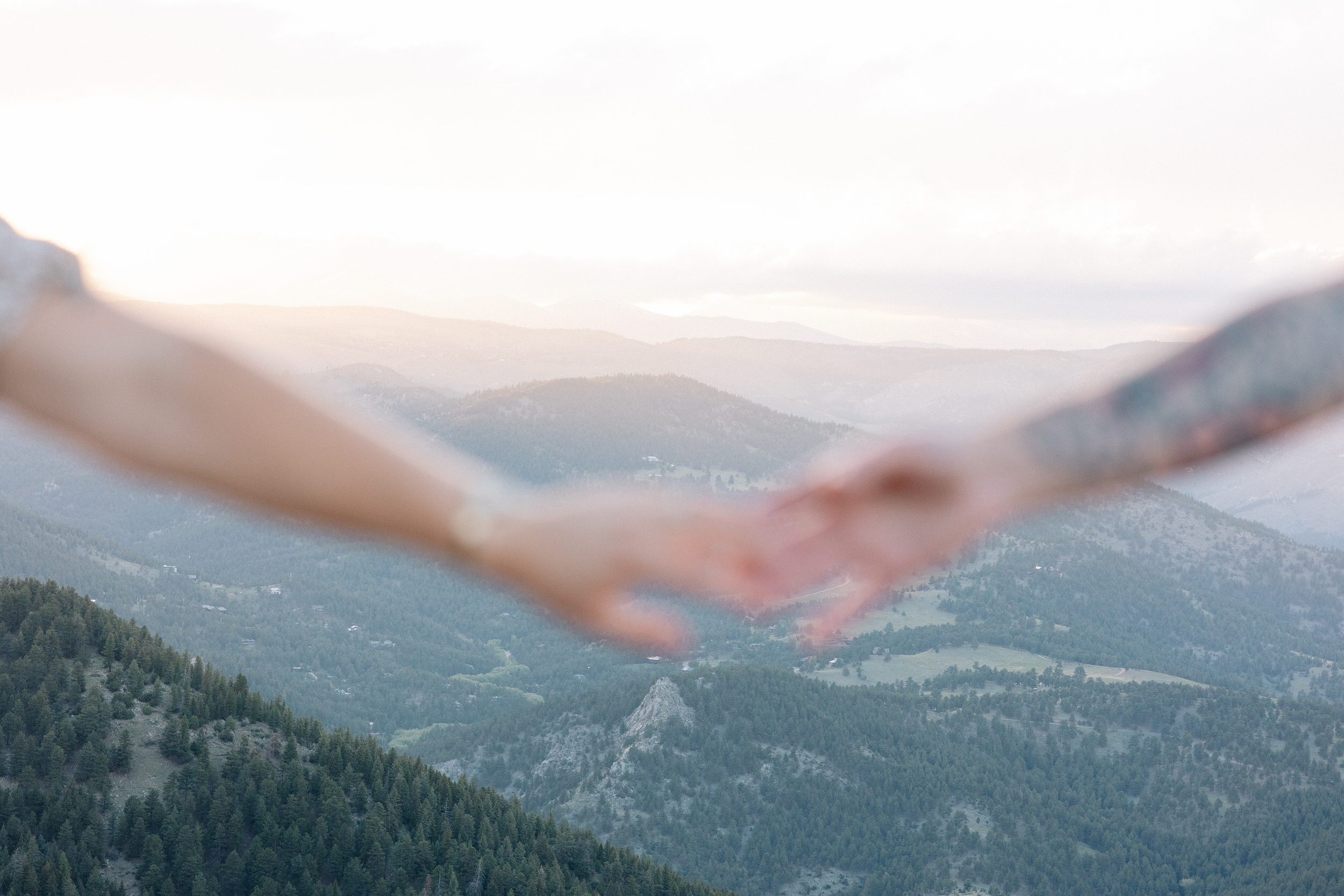 Husband and wife are holding hands, but their hands are out of focus so you can see the mountain view at Lost Gulch Overlook in Boulder, Colorado.